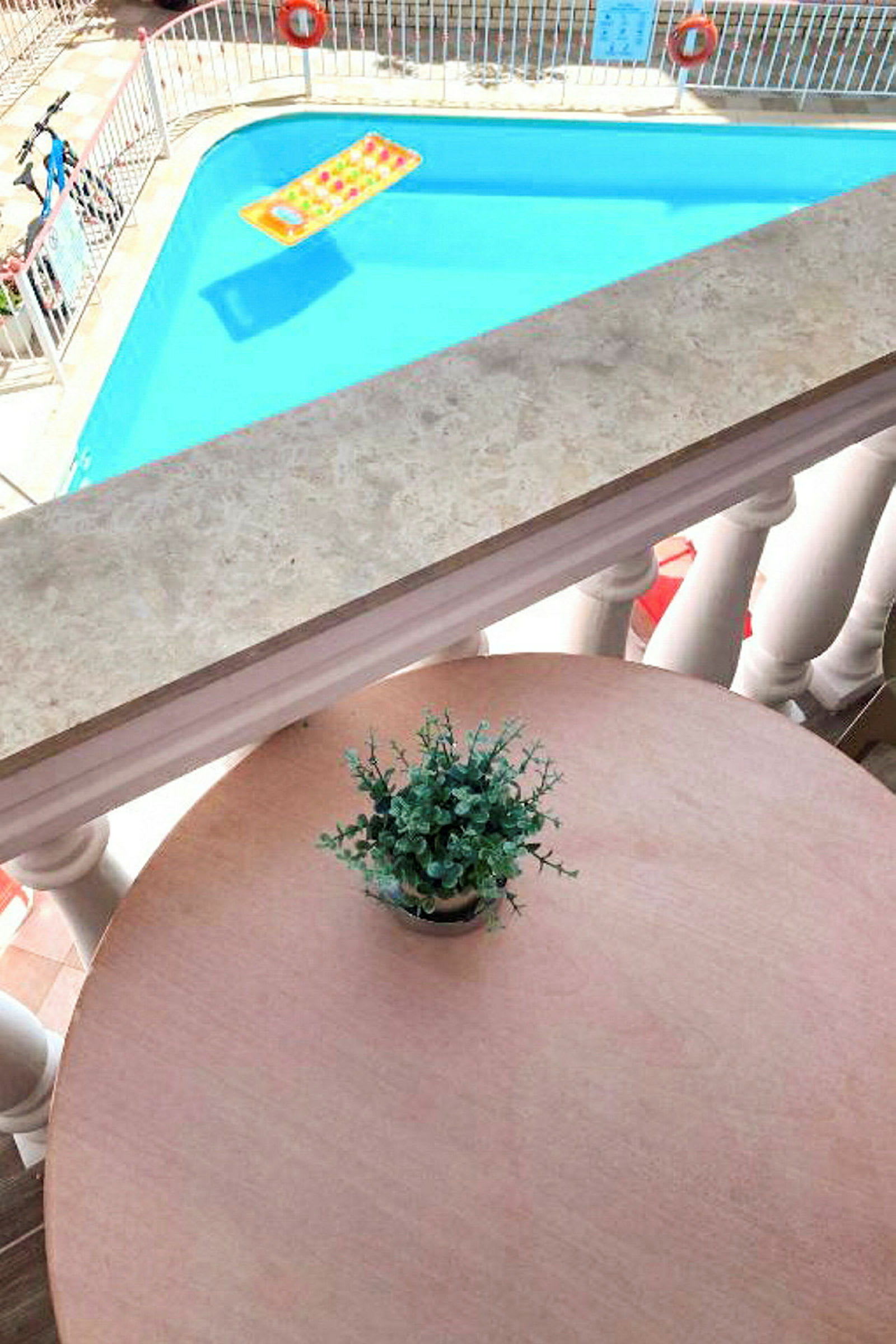 En udsigt fra en altan mod en pool med et badelegetøj og et bord med en urteplante. (AI-genereret tekst)