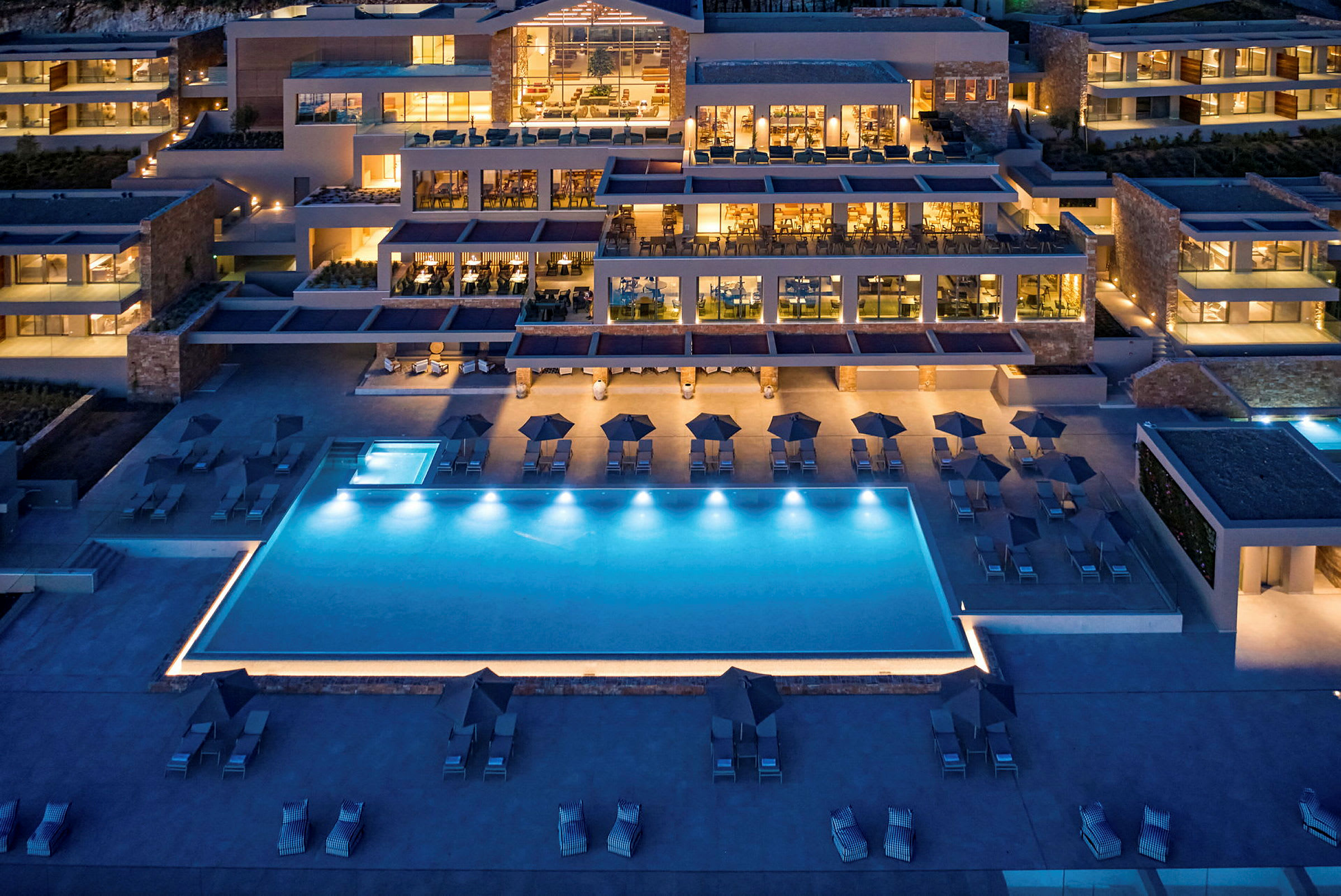 Udsigt over et hotel med pool, udendørsområder og belysning om aftenen. (AI-genereret tekst)