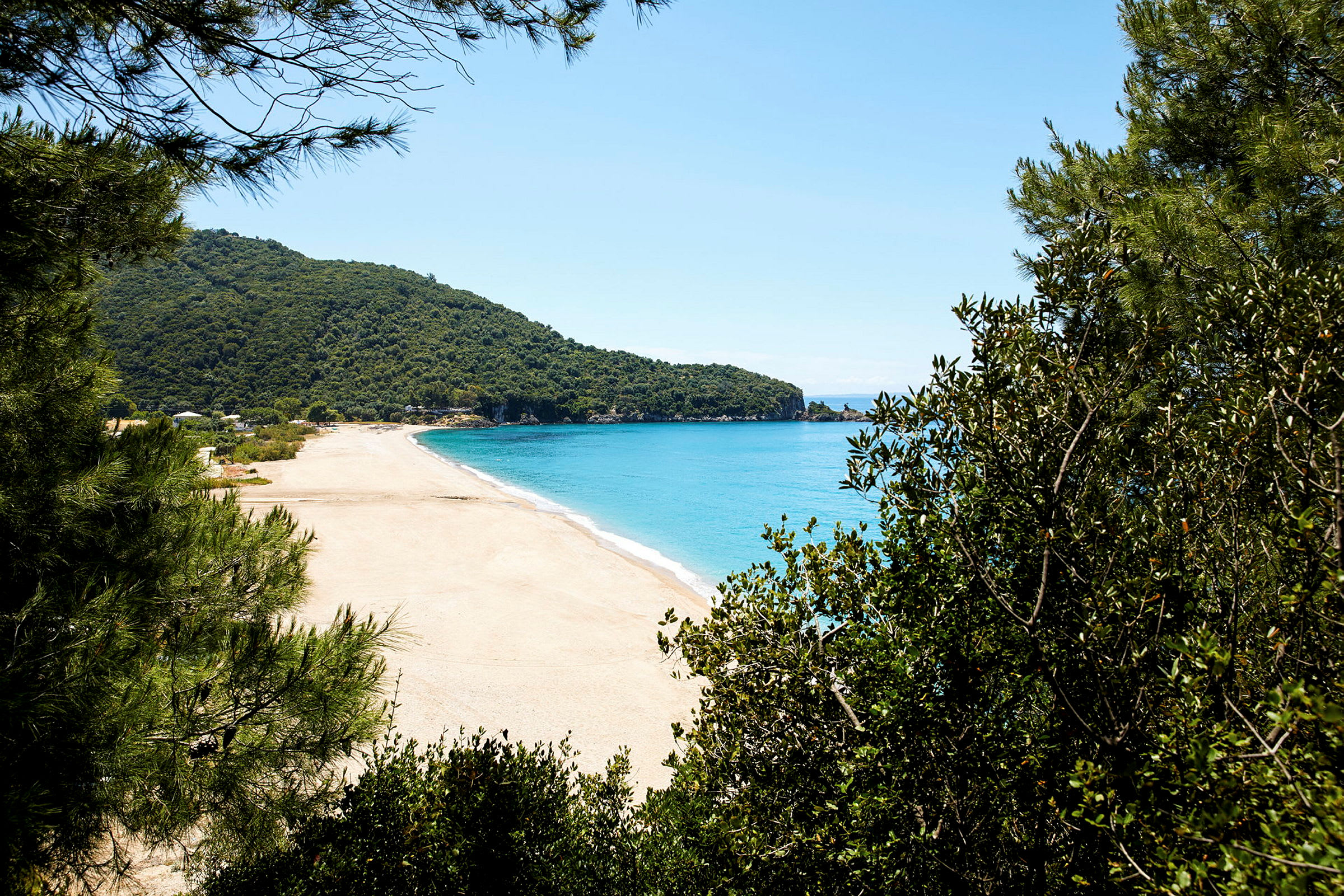 En sandstrand med turkist vand, omgivet af grønne områder og skov. (AI-genereret tekst)
