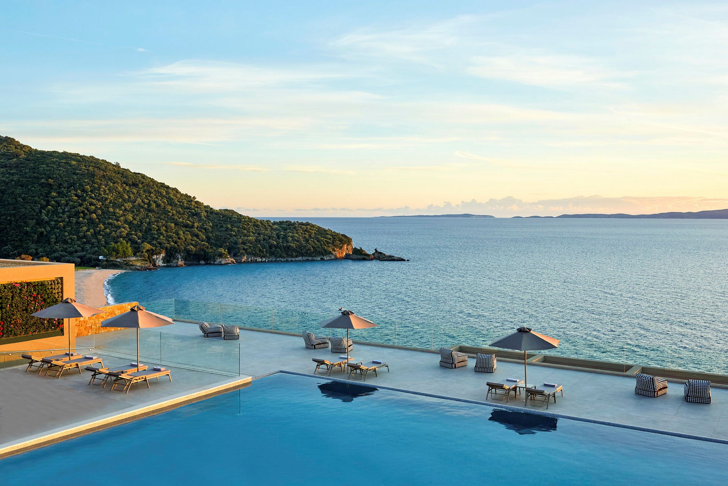 En infinitypool med liggestole og parasoller, med udsigt over havet og en grøn kyst. (AI-genereret tekst)
