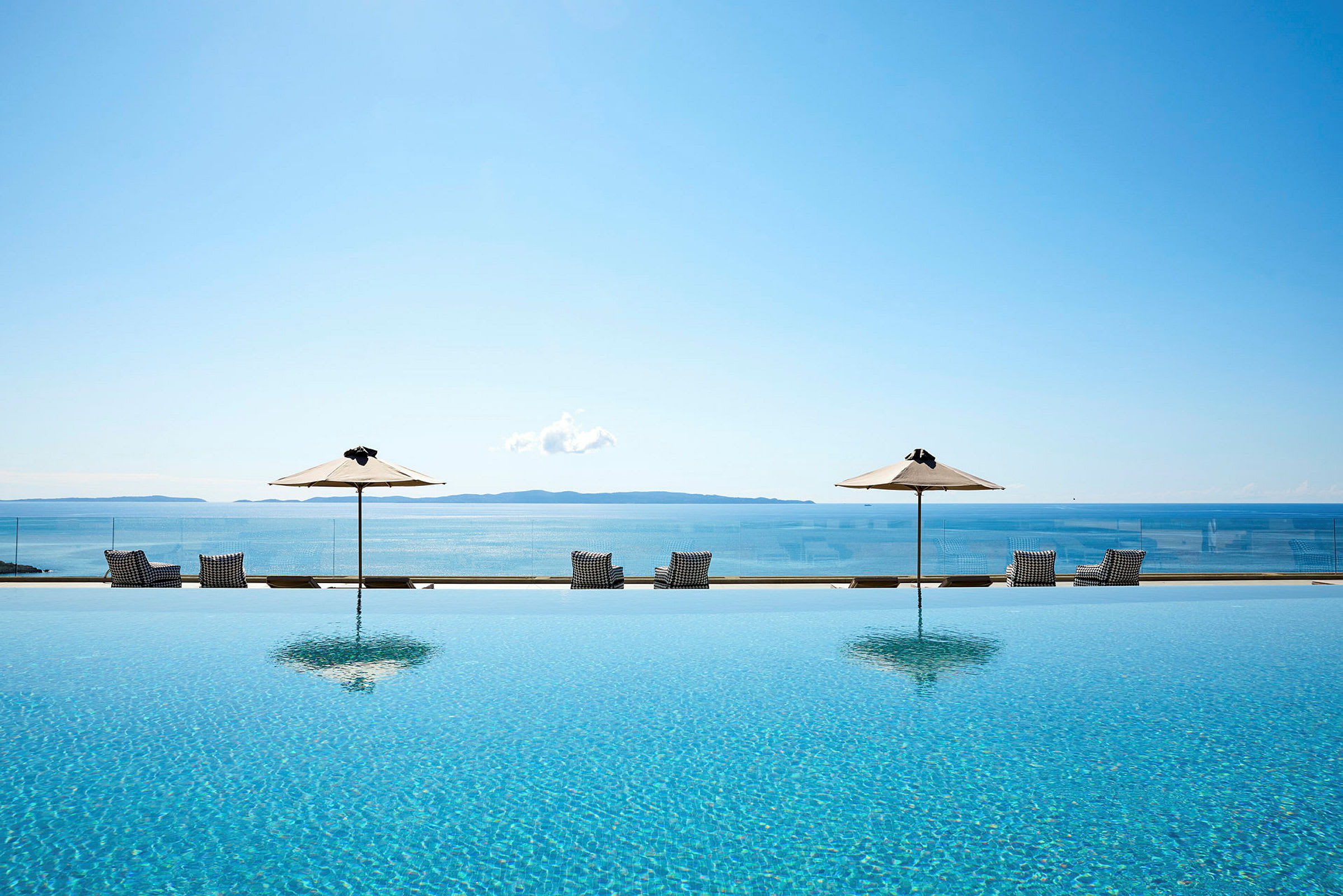 Infinitypool med udsigt over havet, omgivet af liggestole og parasoller. (AI-genereret tekst)