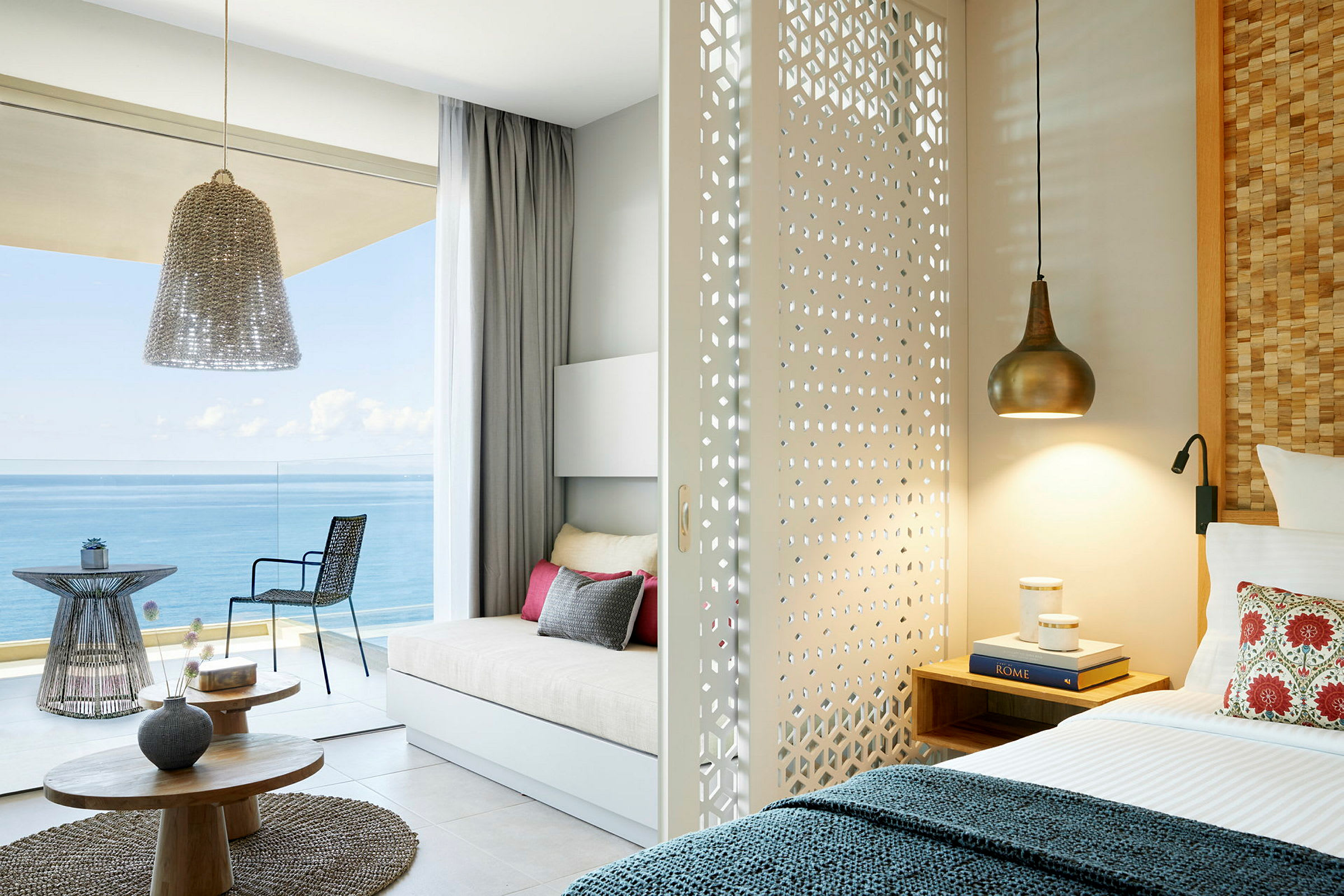 Et lyst hotelværelse med en skydedør dekoreret skillevæg, seng og siddeområde med udsigt over havet. (AI-genereret tekst)