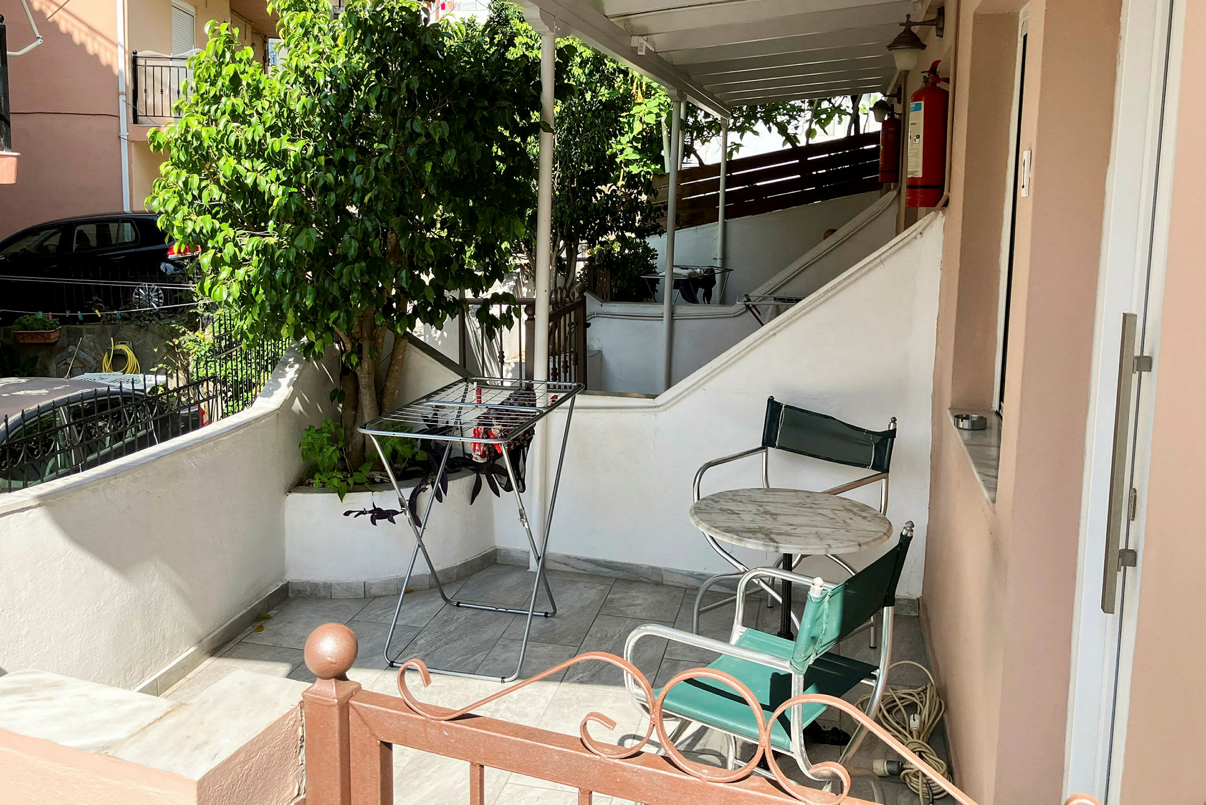 En udendørs terrasse med bord, stole, et tørrestativ og planter. (AI-genereret tekst)
