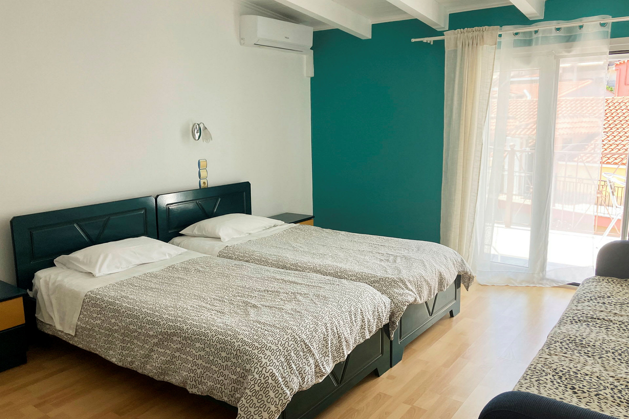 Et hotelværelse med to enkeltsenge, en sofa og en altandør. (AI-genereret tekst)