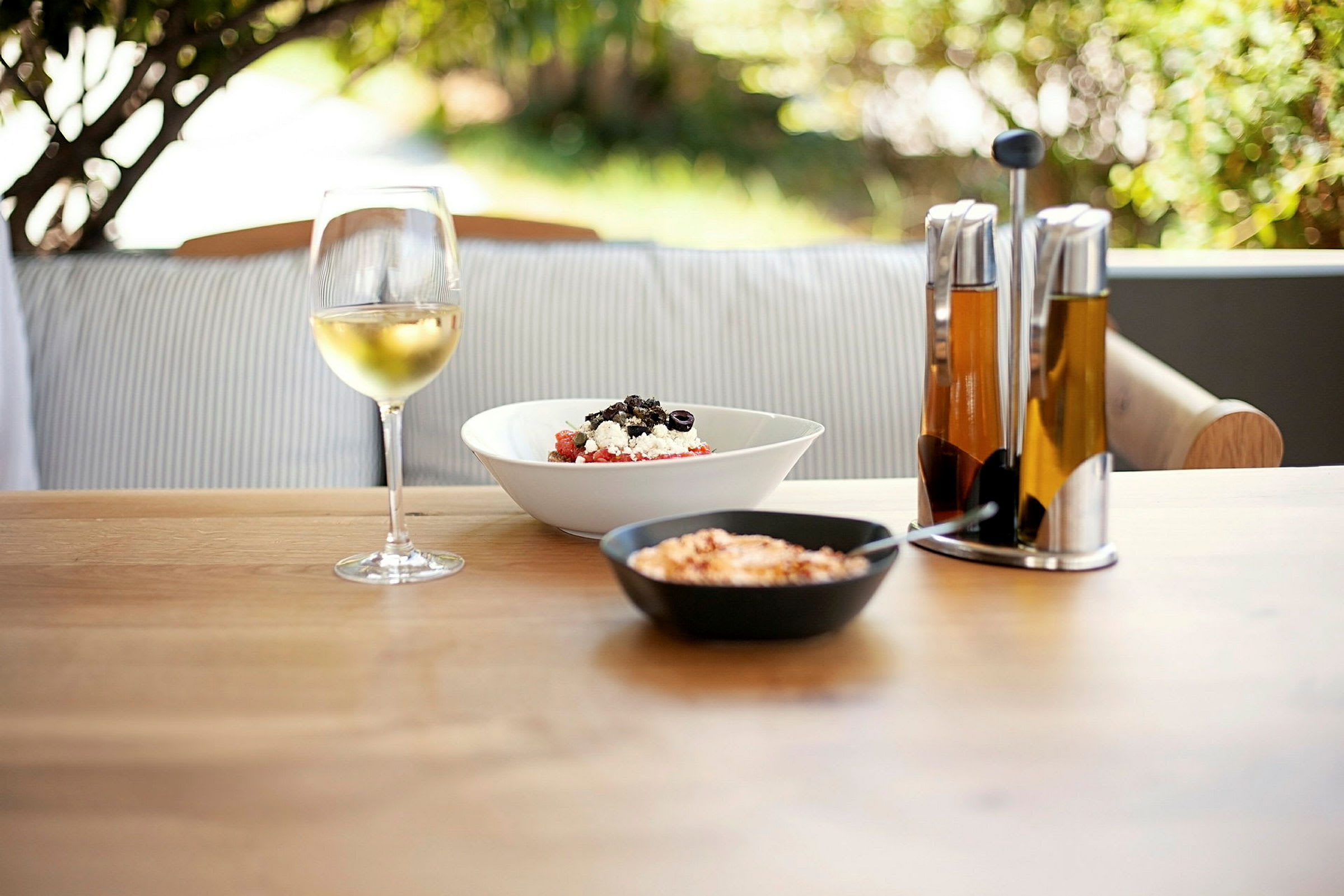Et dækket bord med et glas vin, salat og olieflasker. (AI-genereret tekst)