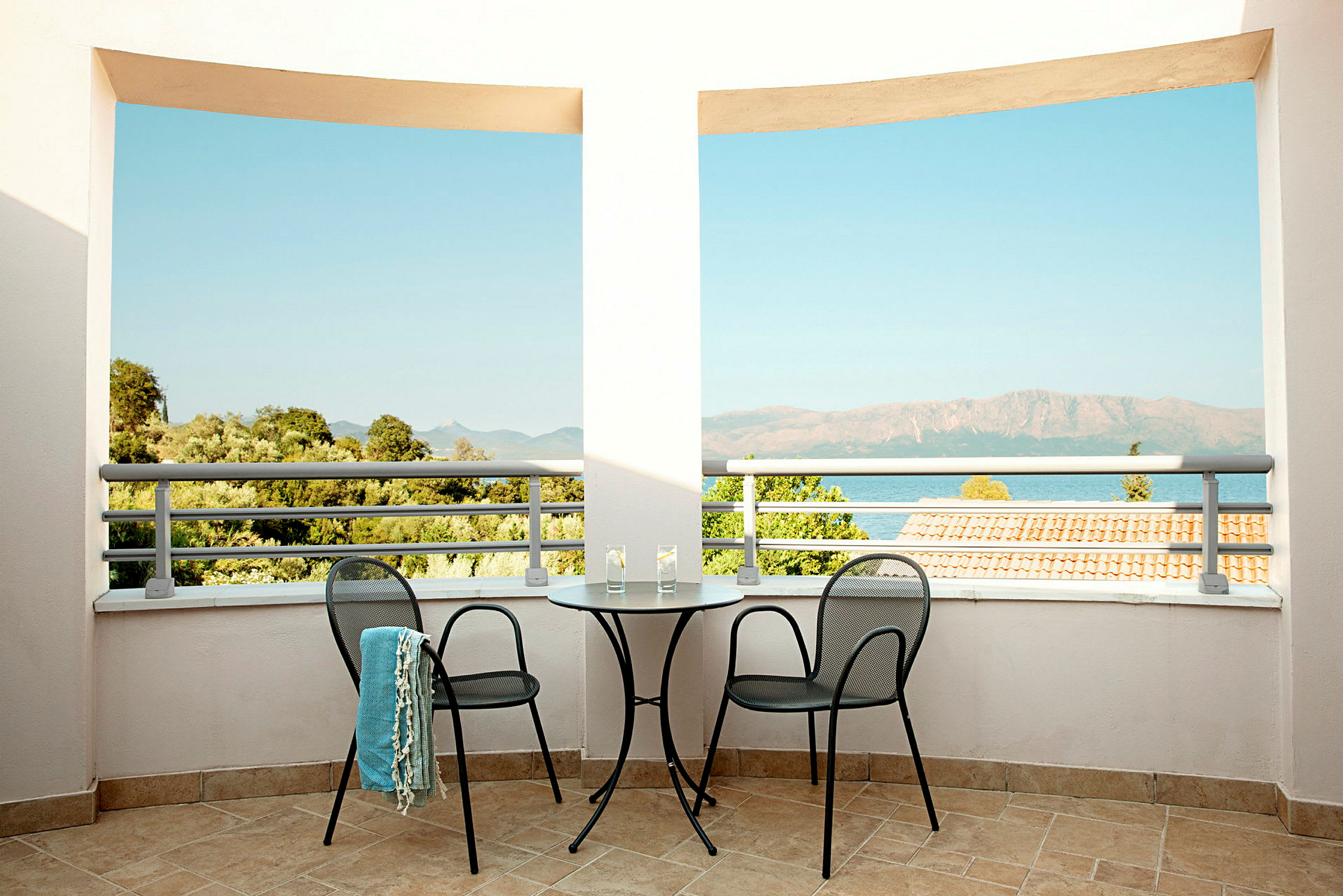 Terrasse med to stole og et bord, udsigt over havet og det omkringliggende landskab. (AI-genereret tekst)
