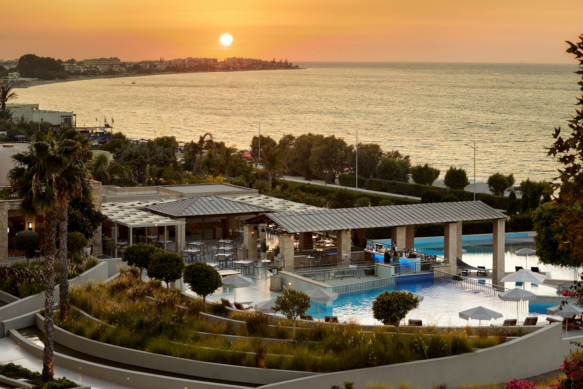 Billede af et hotelområde med en pool og udsigt over havet ved solnedgang. (AI-genereret tekst)