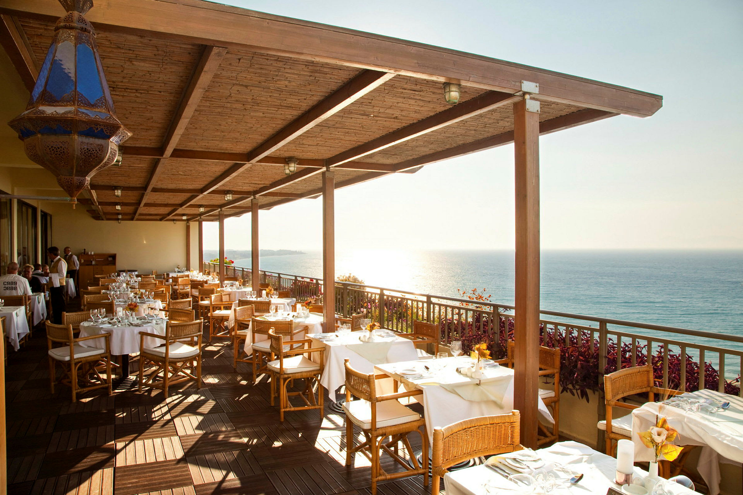 Restaurantterrasse med dækkede borde og havudsigt. (AI-genereret tekst)