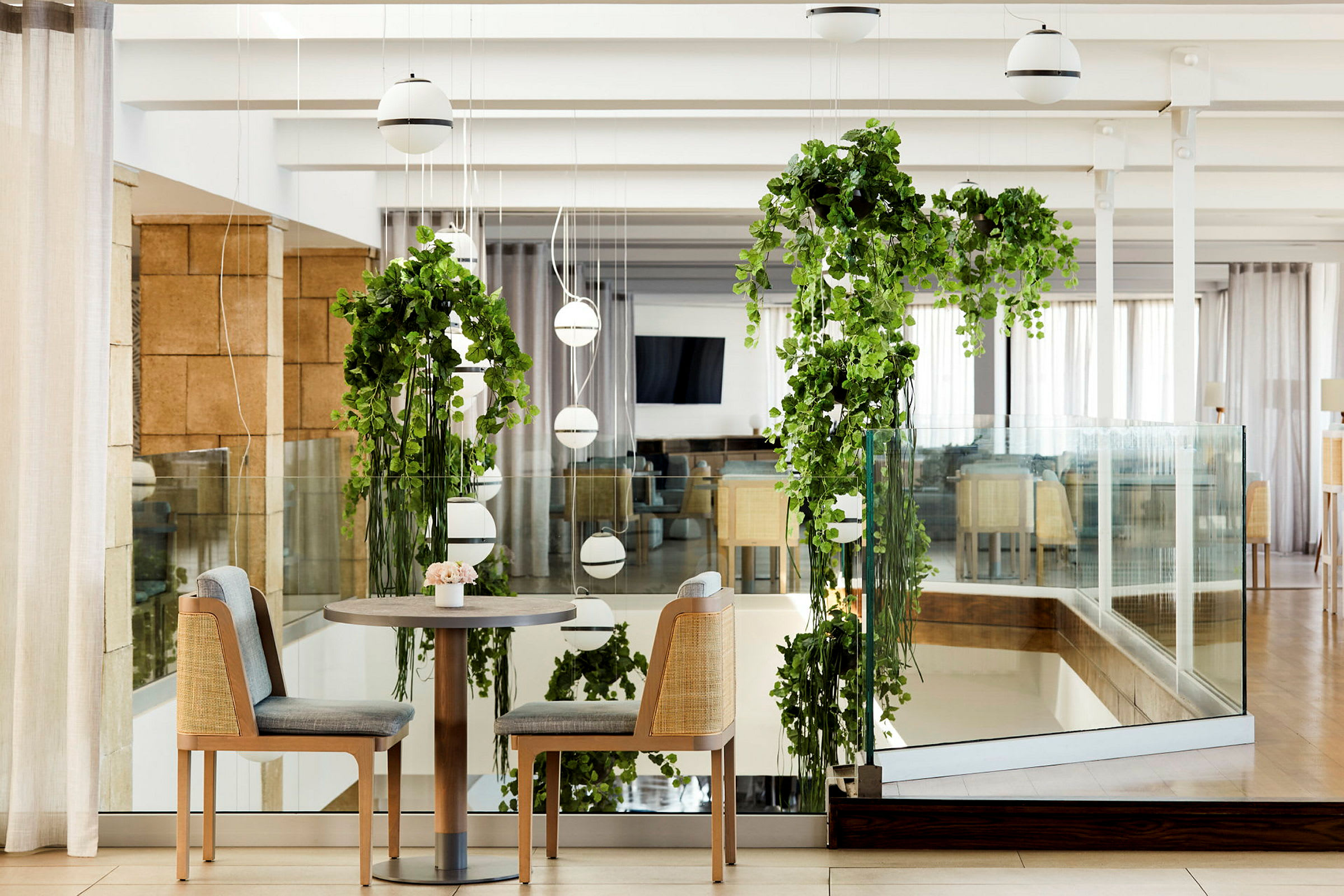 Et par stole ved et bord, omgivet af hængende grønne planter og moderne interiør. (AI-genereret tekst)