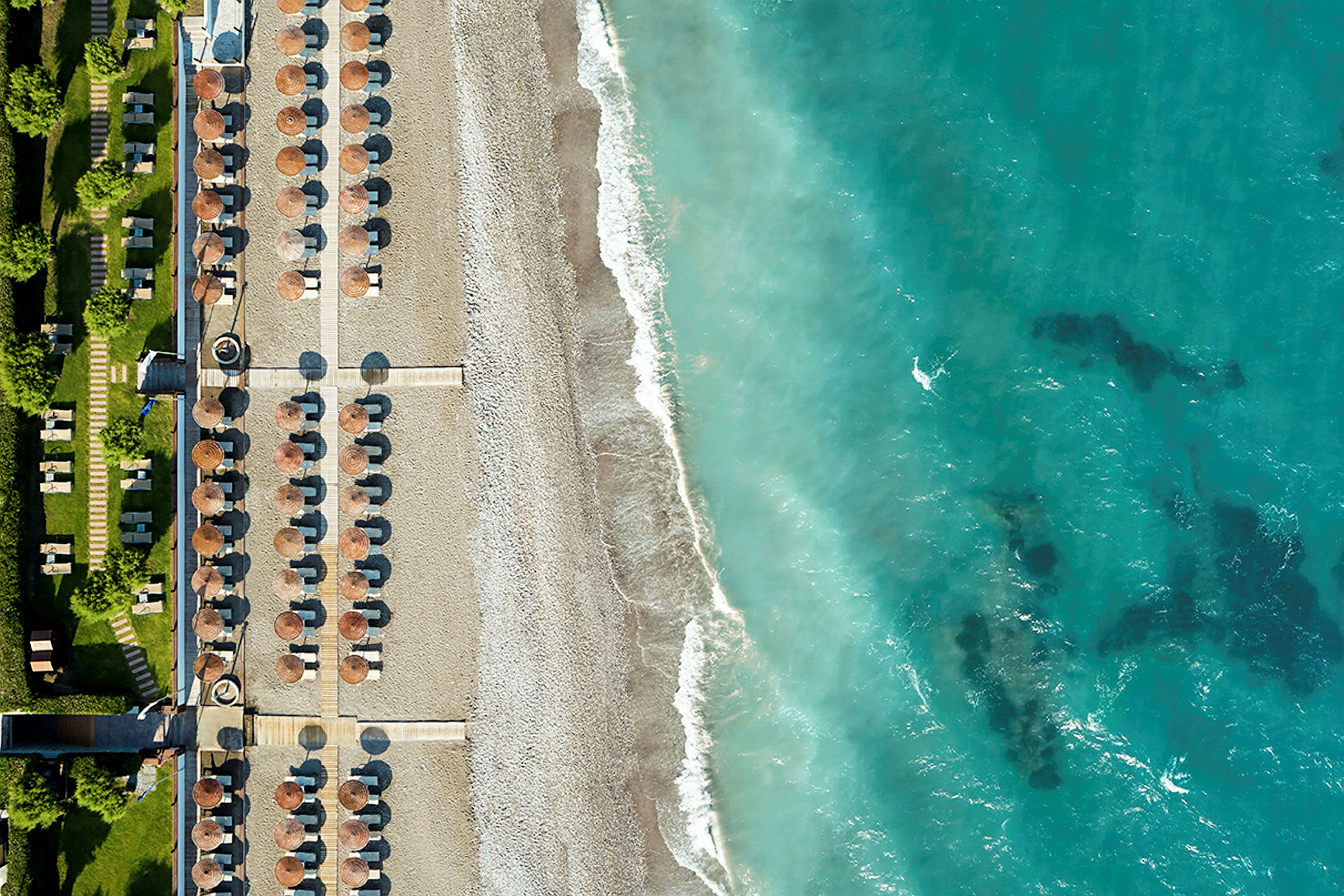 Luftfoto af en strand med parasoller og solsenge ved siden af en turkisblå havsstrand. (AI-genereret tekst)
