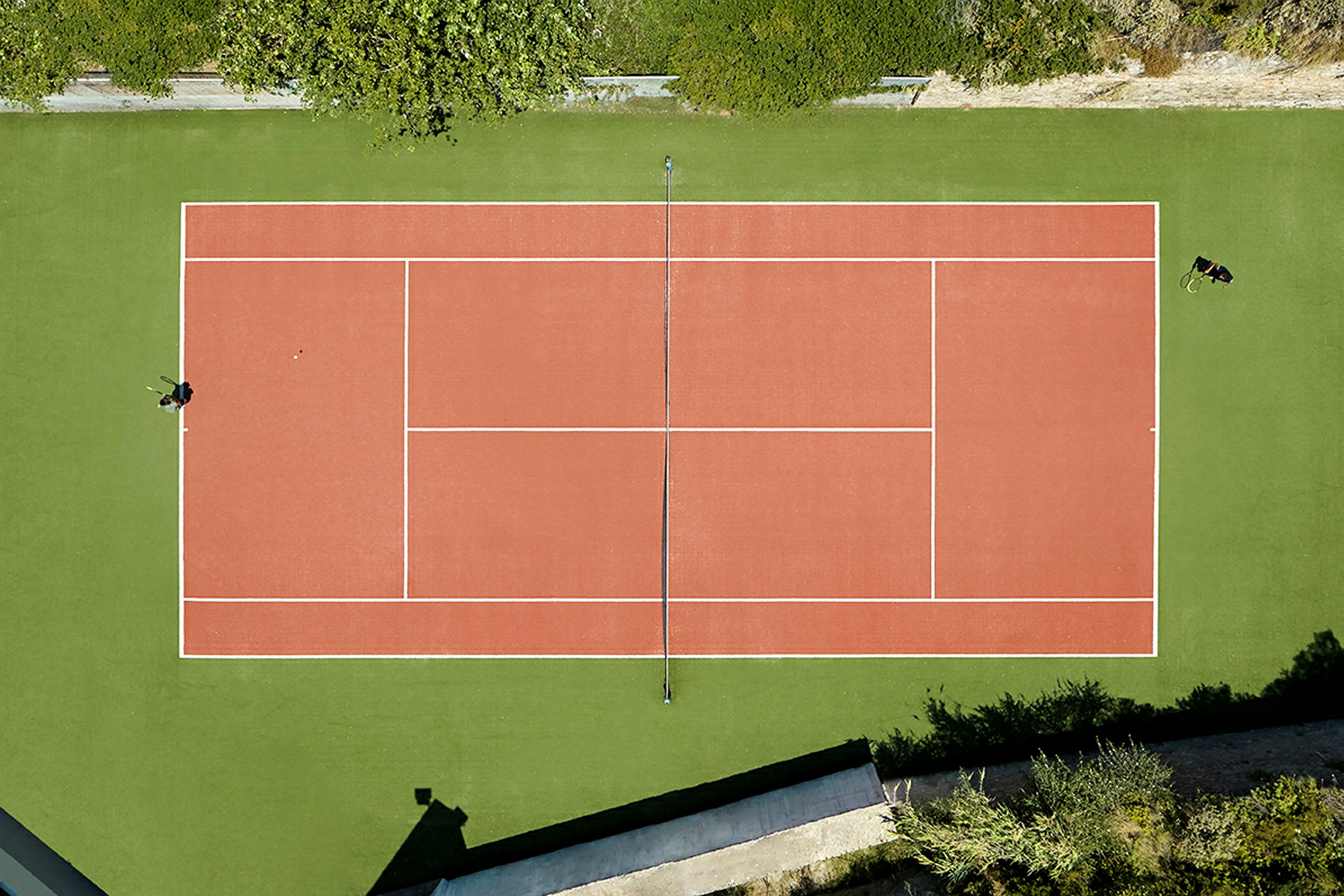 En tennisbane set ovenfra med grøn omgivelser. (AI-genereret tekst)