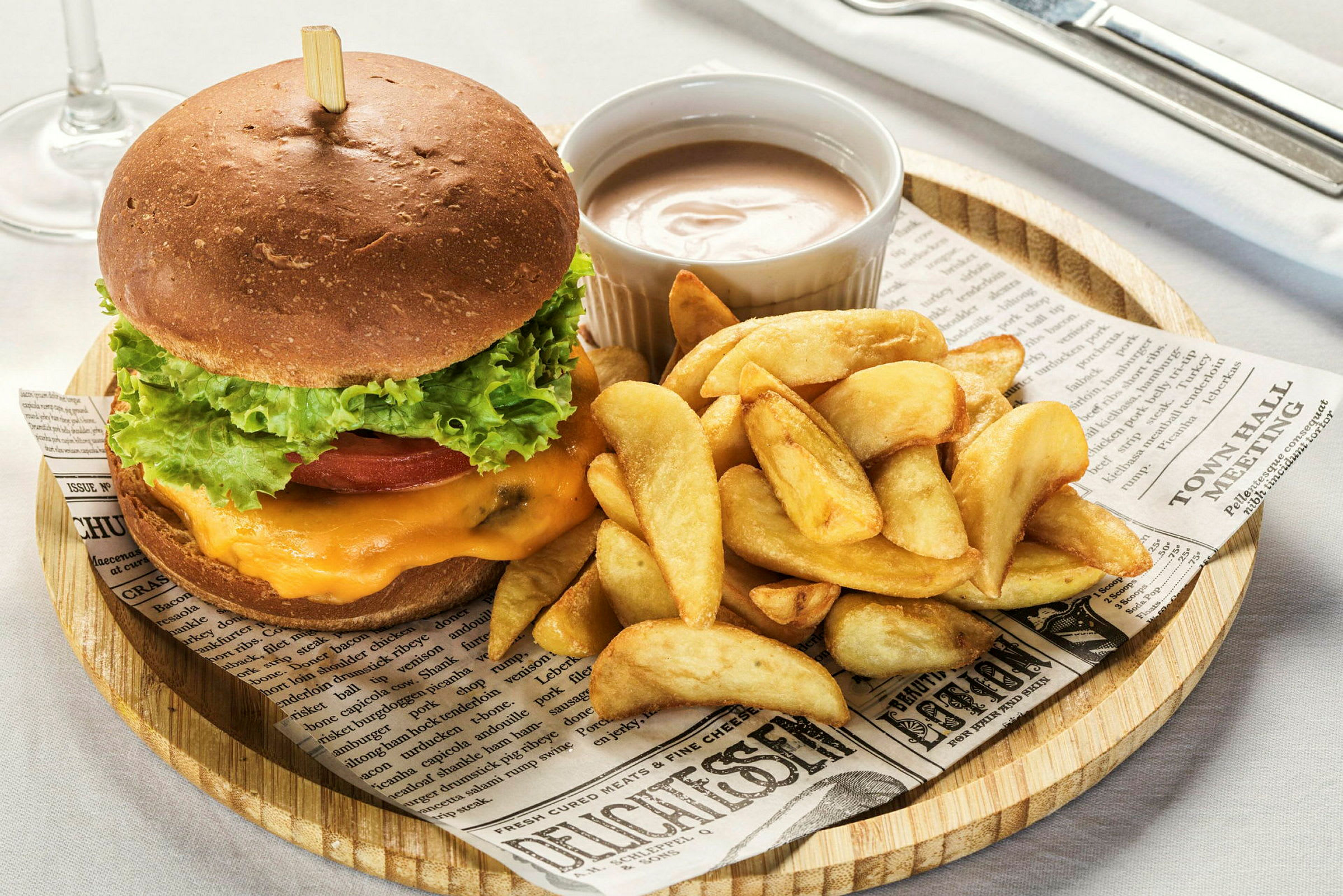 En burger med salat, tomat og ost serveret med kartoffelbåde og en dip. (AI-genereret tekst)