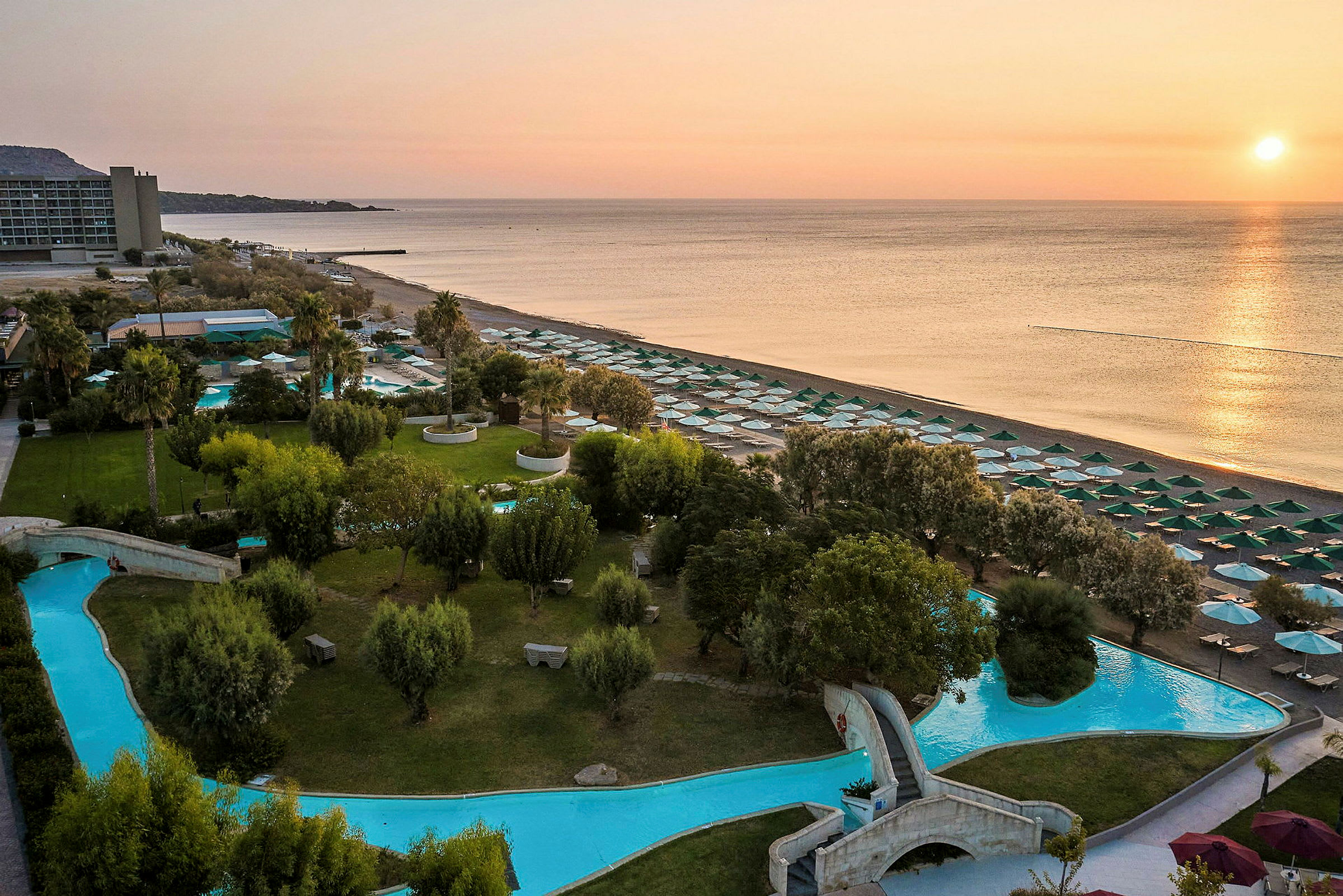En strand og hotelområde med pools og grønne områder ved solnedgang. (AI-genereret tekst)
