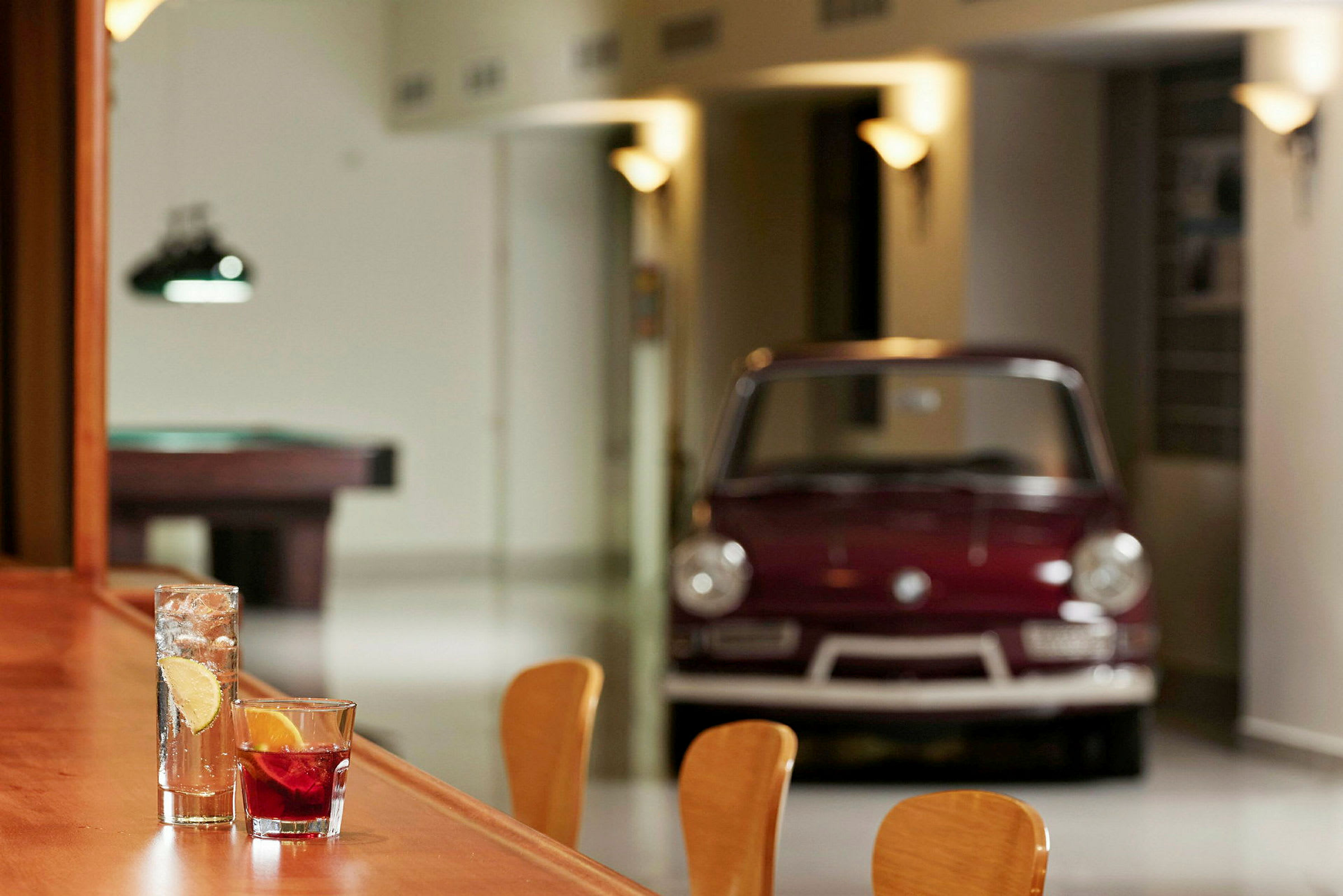 To drinks står på et træbord, med en klassisk bil og et billardbord i baggrunden. (AI-genereret tekst)