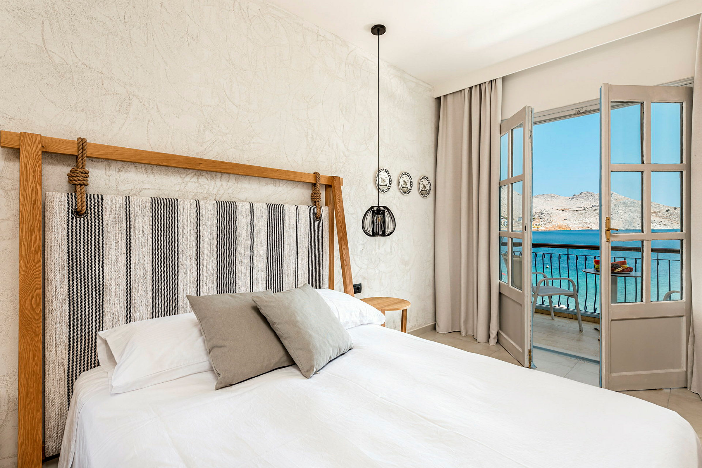 Soveværelse med en dobbeltseng og en åbning mod en balkon med udsigt over havet. (AI-genereret tekst)