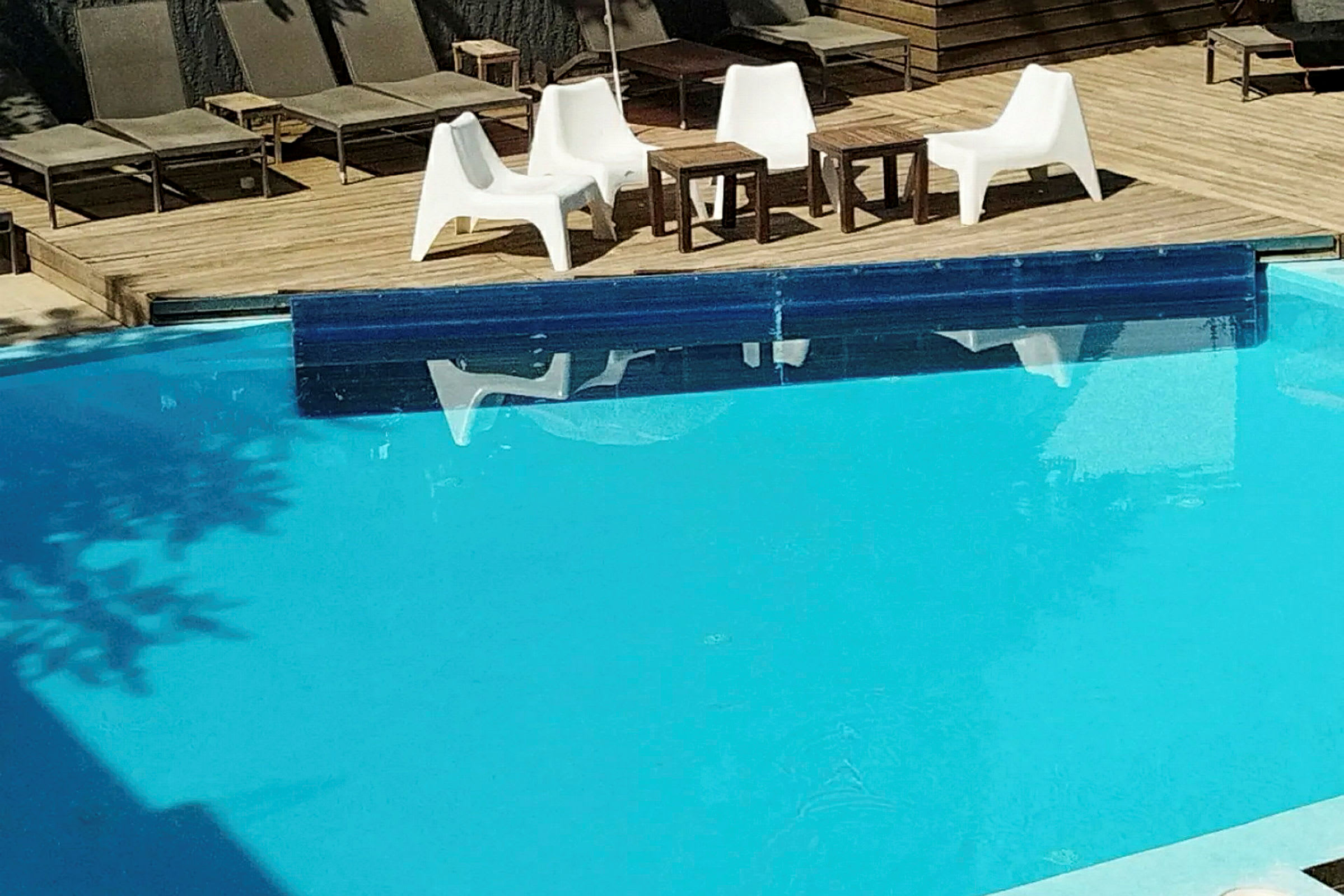 Trædæk ved en pool med flere liggestole og en siddegruppe. (AI-genereret tekst)