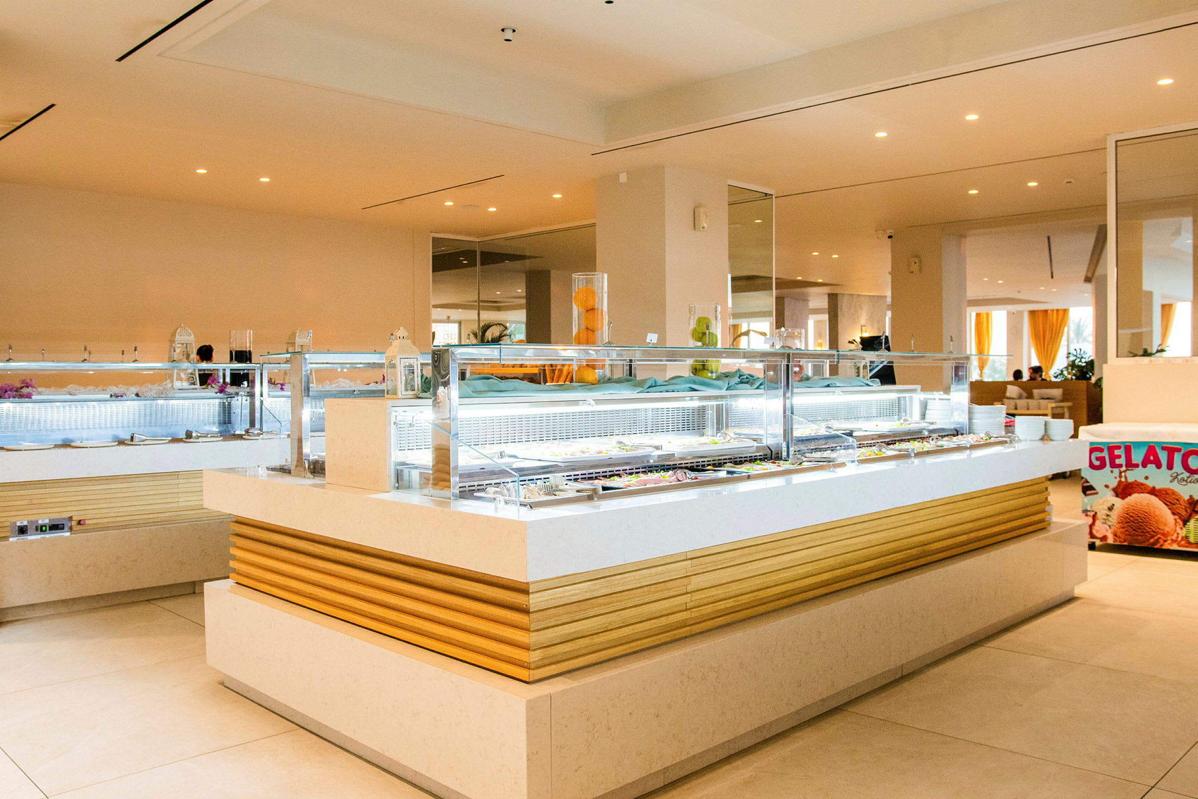 Et billede af en moderne buffetstation med et isskilt, der viser "Gelato", og en glasdisk med forskellige madmuligheder. (AI-genereret tekst)