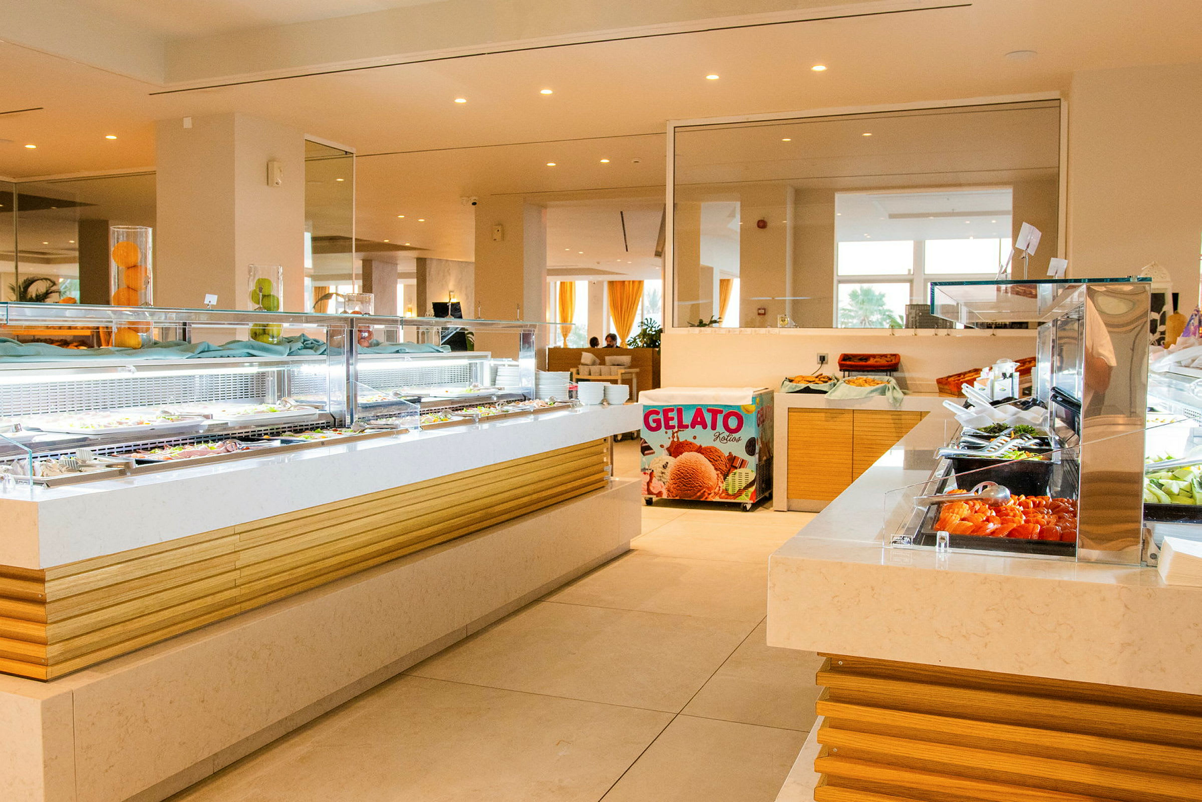 Billede af en hotelbuffet med flere madstationer fyldt med forskellige retter og en gelatosalgsdisk synlig i baggrunden. (AI-genereret tekst)