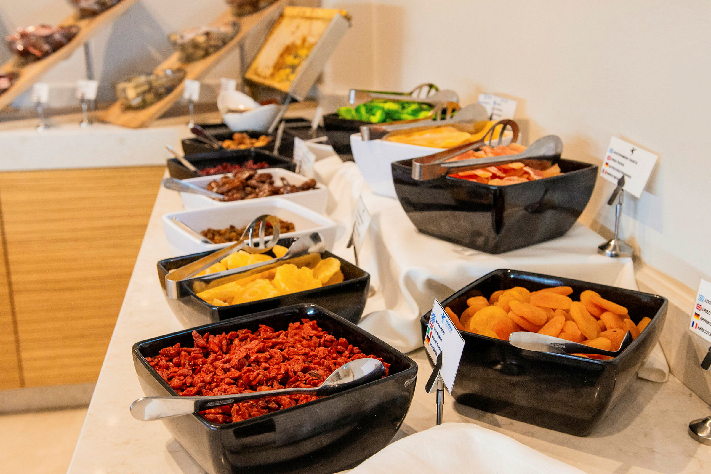 En buffet med forskellige tørrede frugter og friske fødevarer i sorte og hvide skåle på et dækket bord. (AI-genereret tekst)