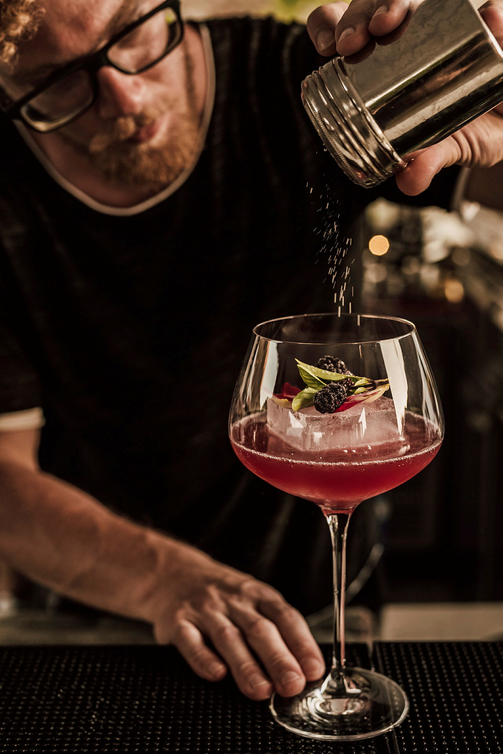 En hånd drysser pulver over en cocktail pyntet med bær og blade. (AI-genereret tekst)