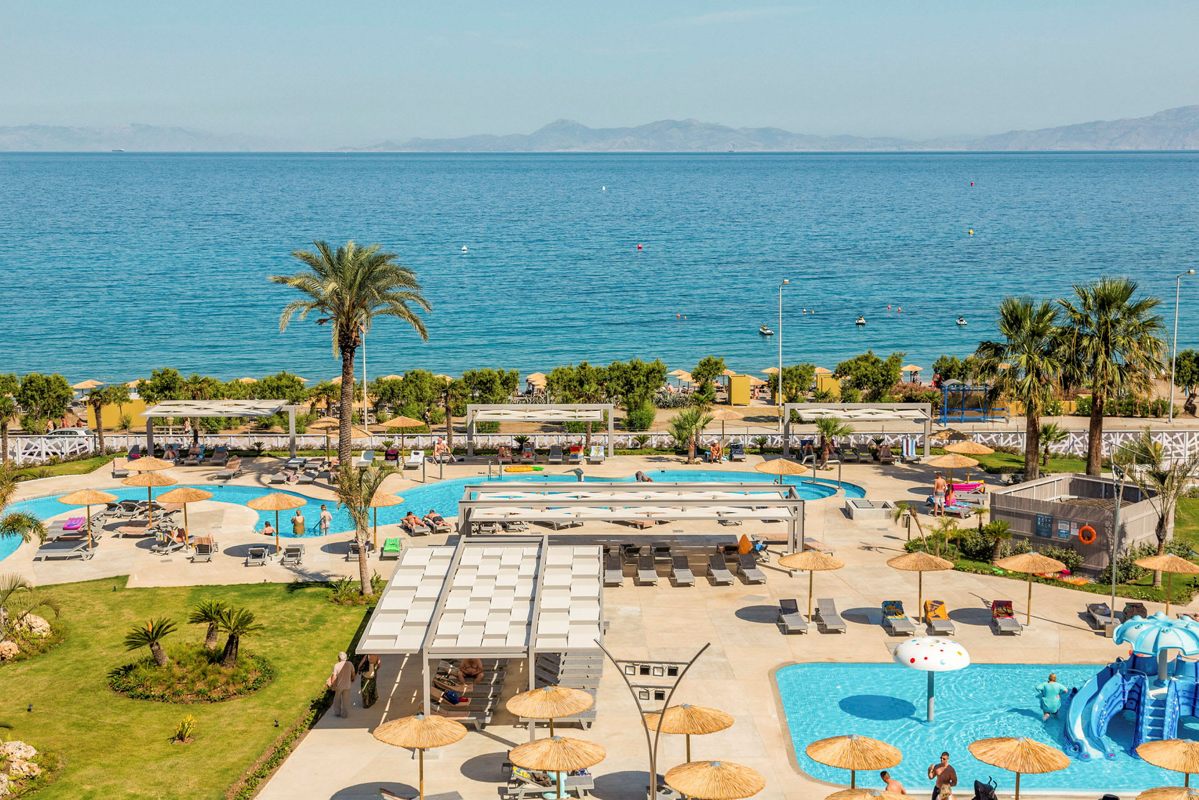 En udsigt over hotelområdet med swimmingpools og liggestole, havet ses i baggrunden. (AI-genereret tekst)