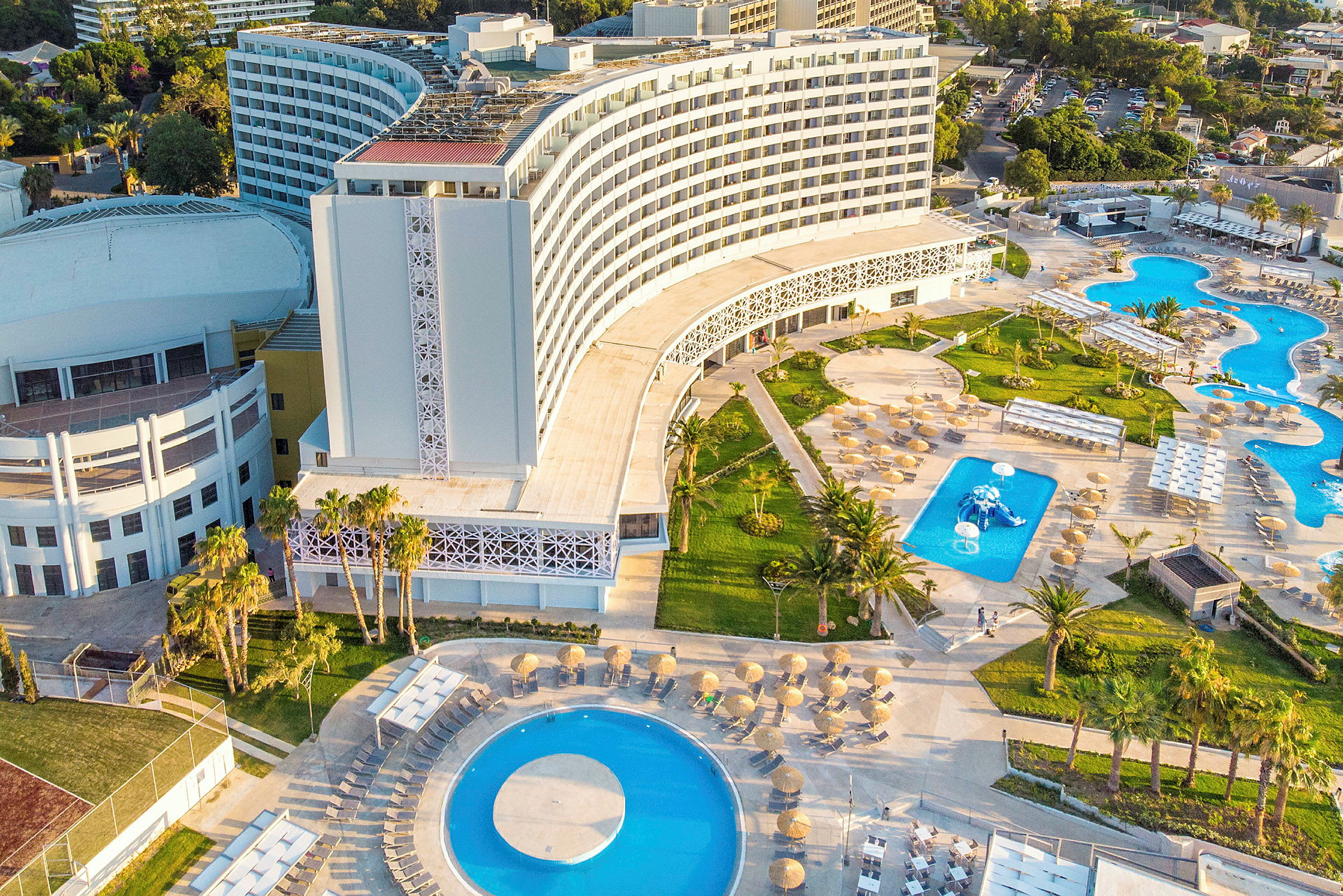 Luftfoto af et moderne hotel med swimmingpools og grønne områder. (AI-genereret tekst)