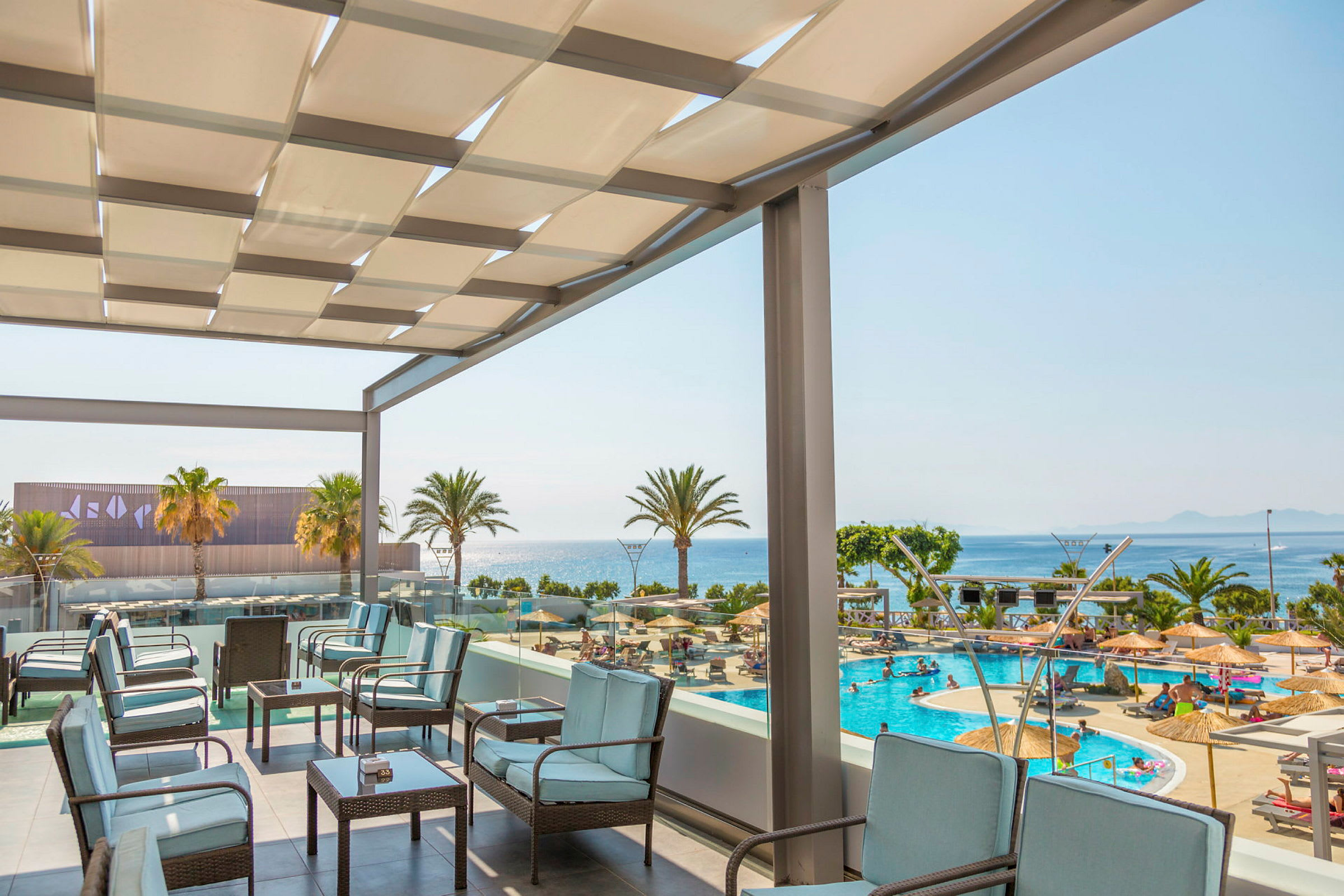 Udendørs terrasse med siddepladser og udsigt over et poolområde og havet. (AI-genereret tekst)