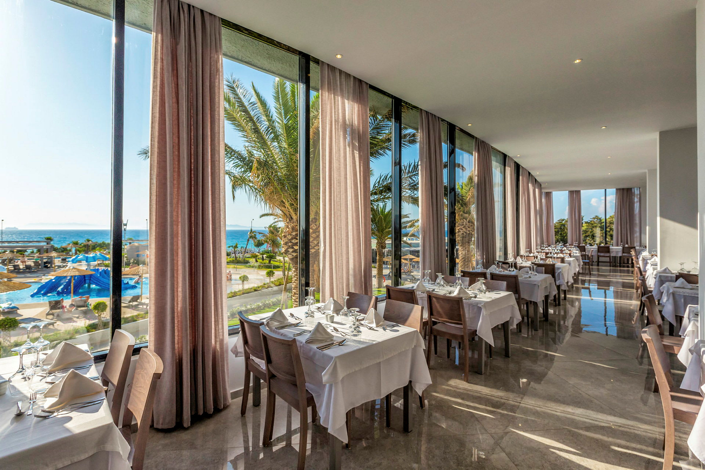 Restaurant med dækkede borde og udsigt over pool og hav. (AI-genereret tekst)