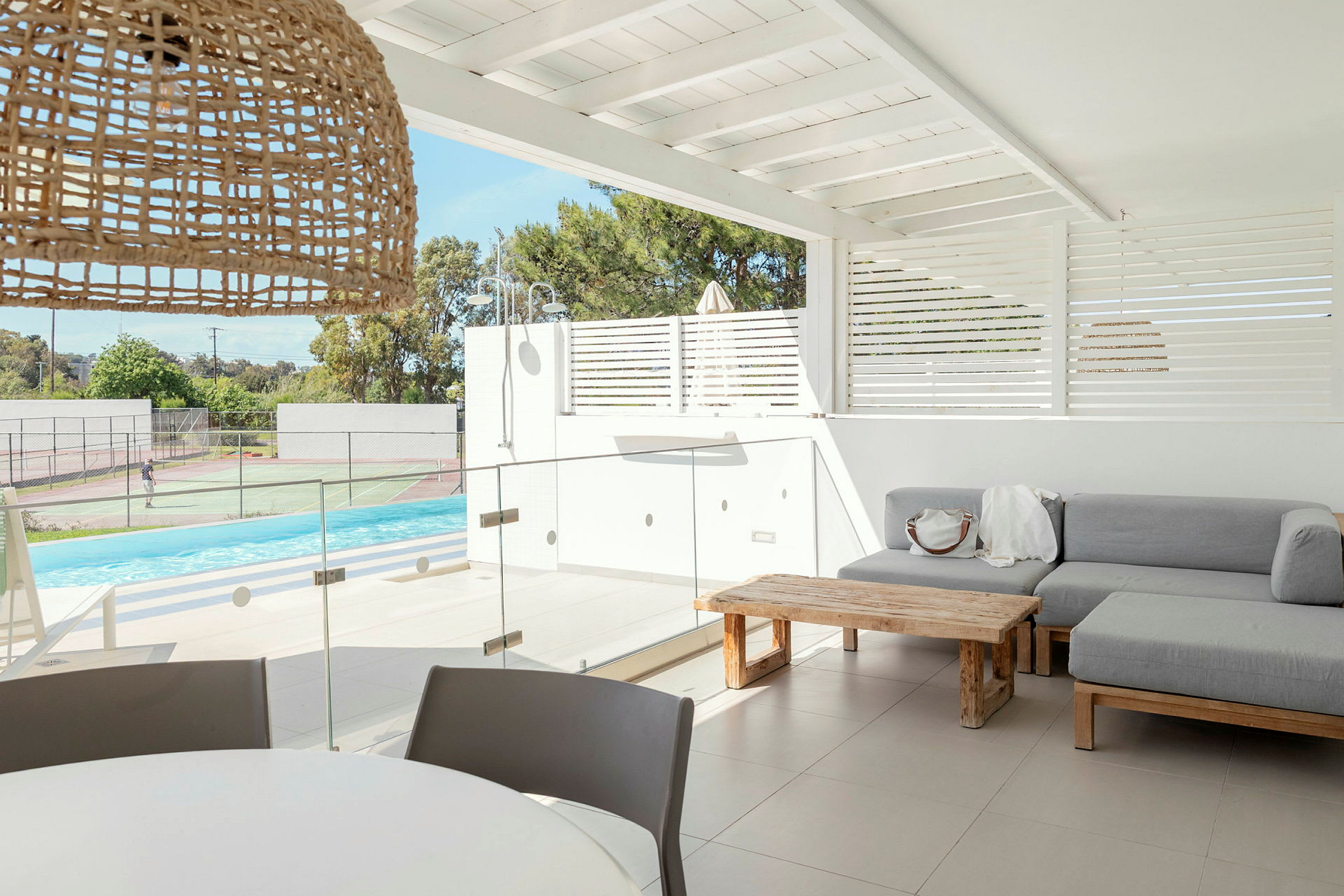 En moderne terrasse med sofa, bord og udsigt over pool og tennisbaner. (AI-genereret tekst)