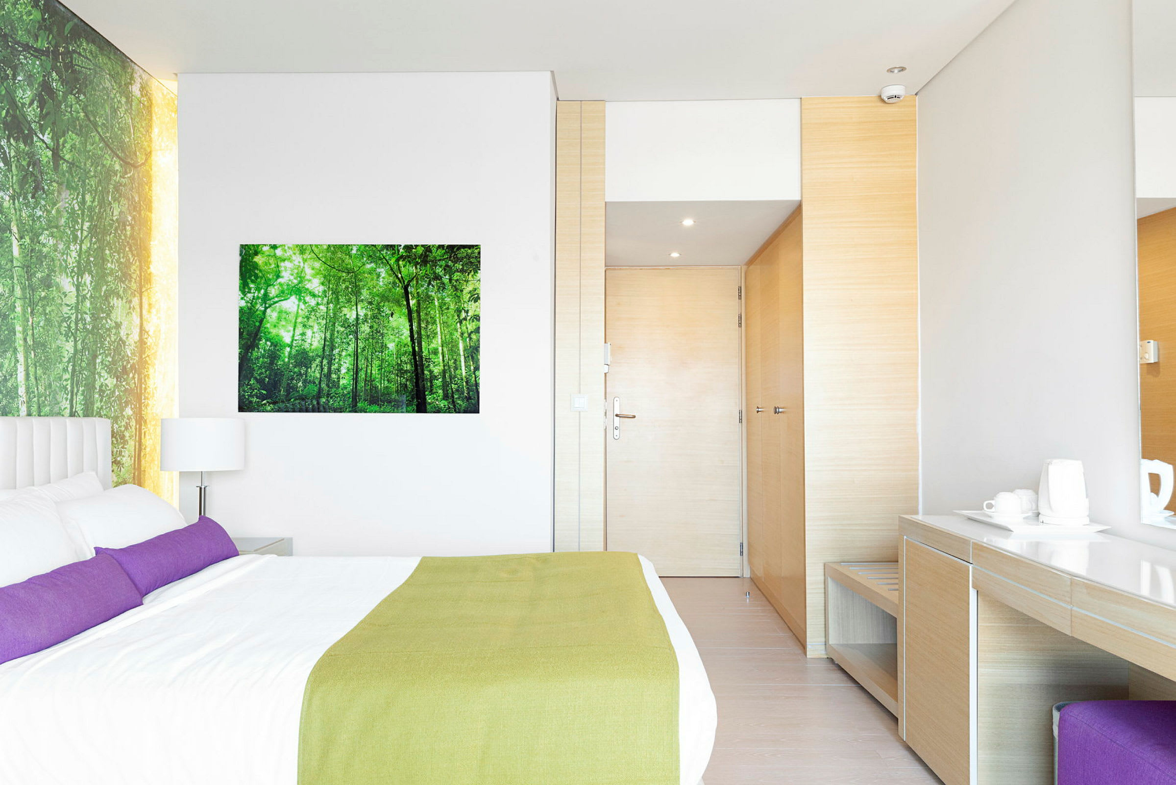 Billede af et moderne hotelværelse med en dobbeltseng, skrivebord og garderobe. Væggen er dekoreret med et naturbillede. (AI-genereret tekst)