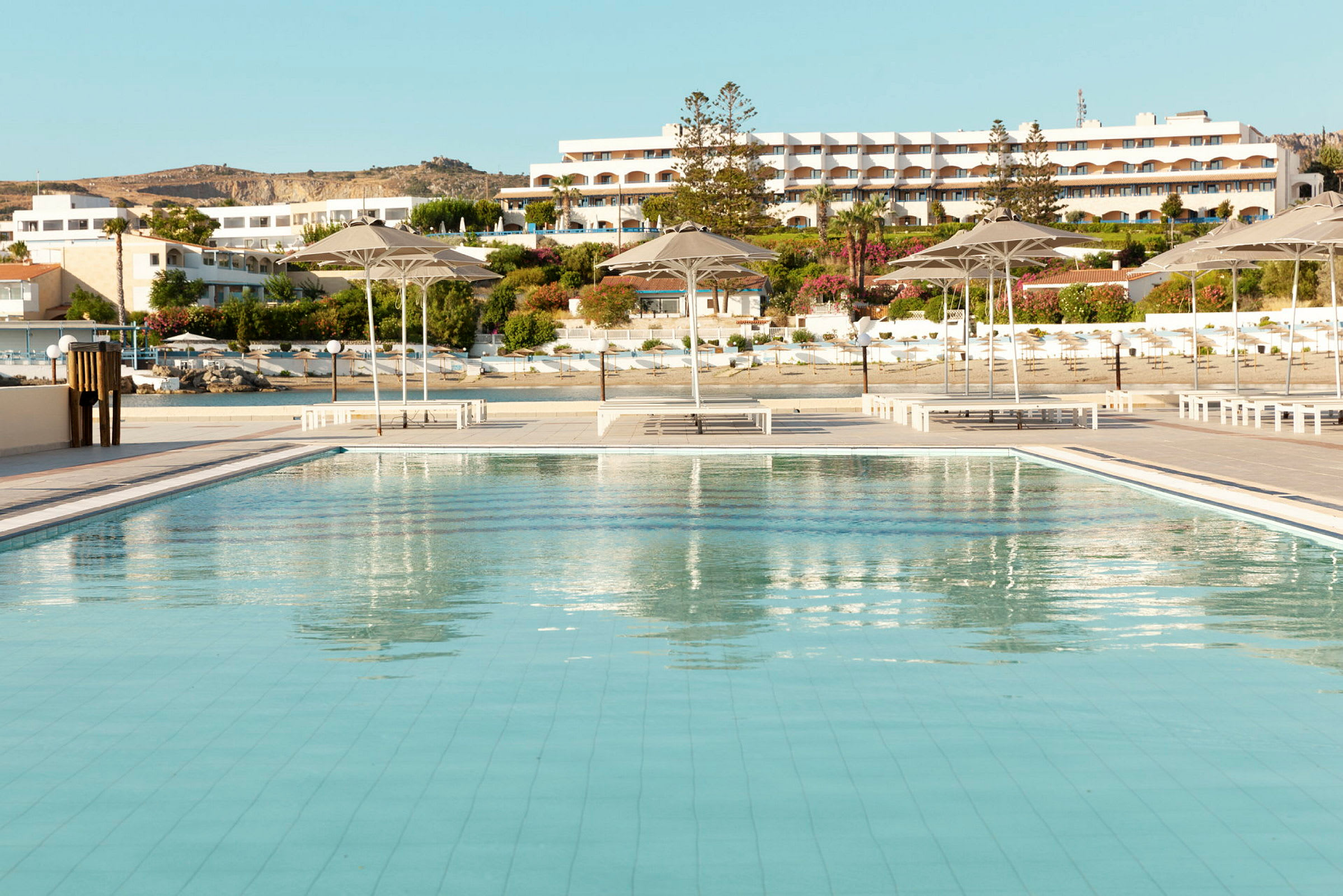 Stor swimmingpool med parasoller og hotelbygninger i baggrunden. (AI-genereret tekst)