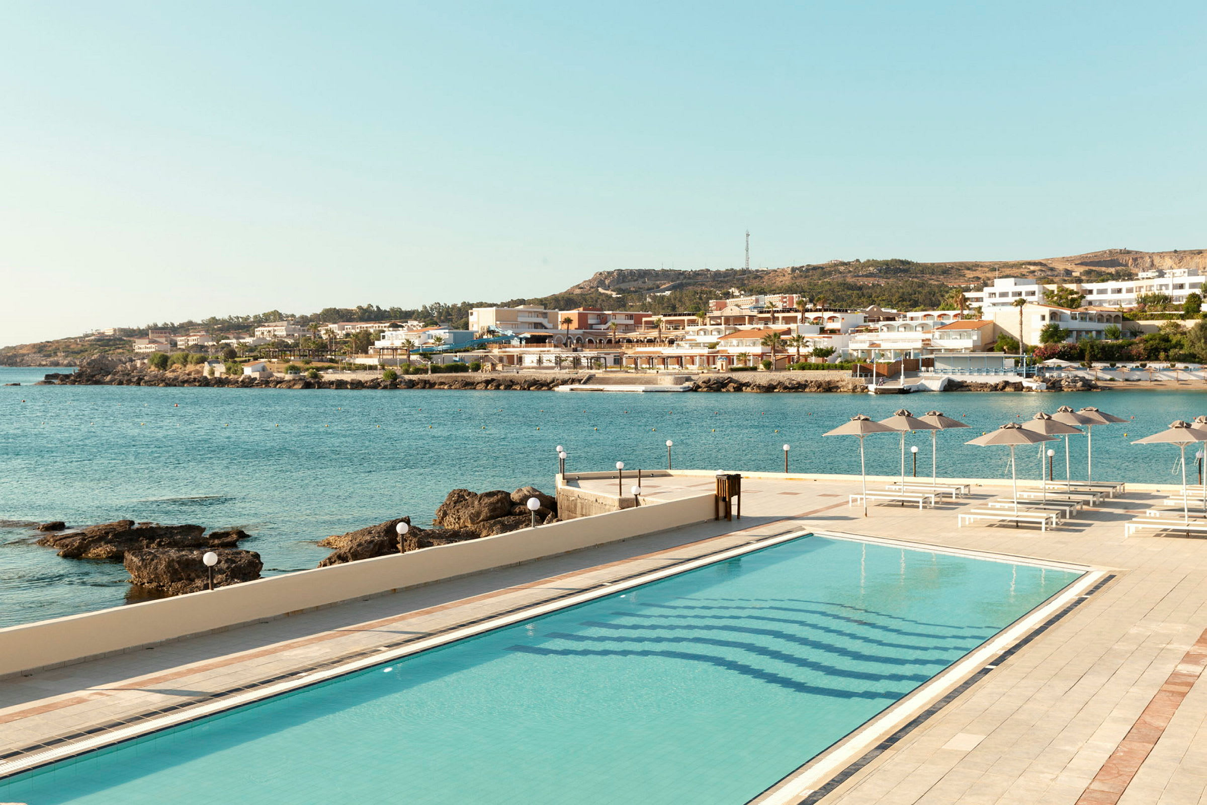 Billede af en pool med udsigt over havet og en kystby. (AI-genereret tekst)