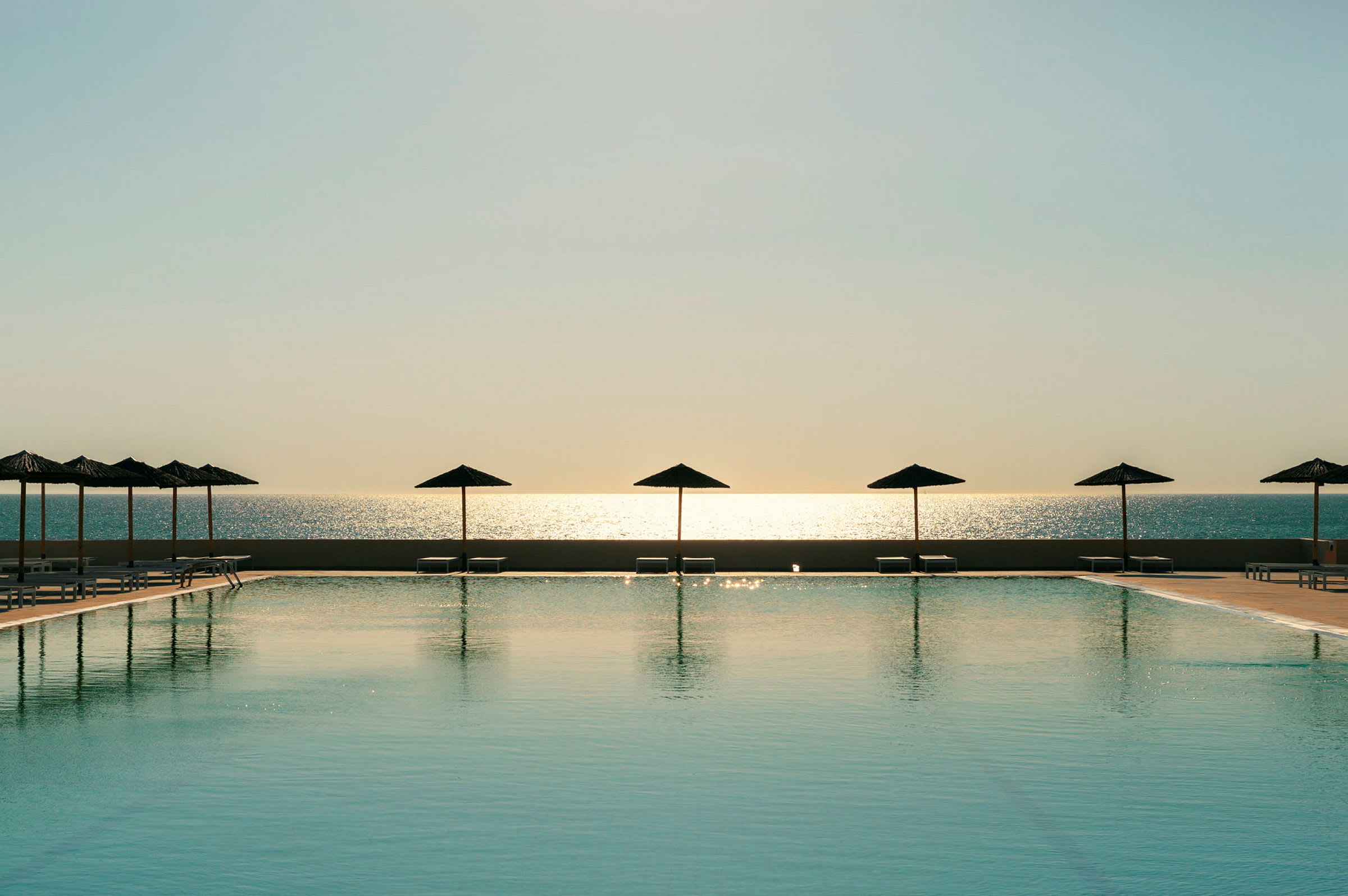 En pool med parasoller foran havet ved solnedgang. (AI-genereret tekst)