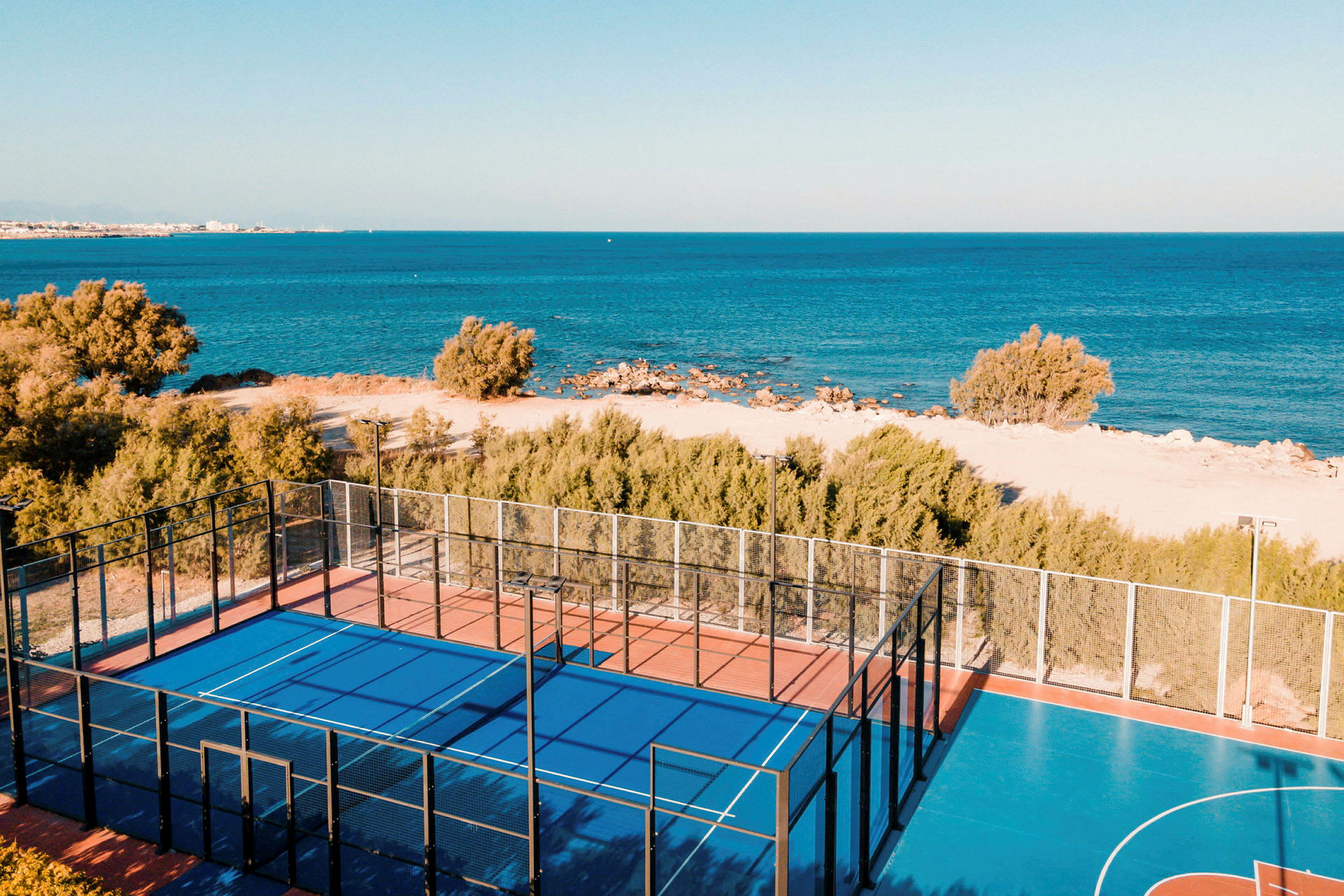 Padelbane med blåt underlag tæt ved stranden og havet. (AI-genereret tekst)