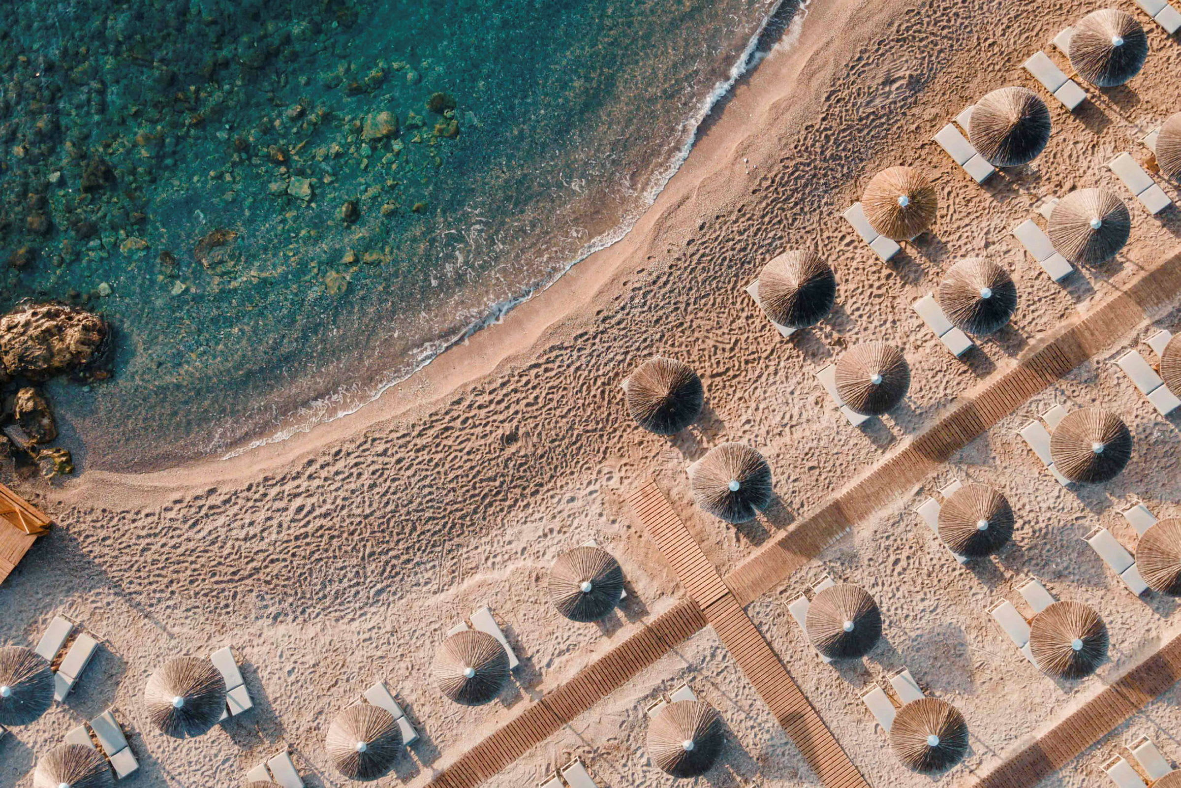 Luftfoto af en sandstrand med parasoller og liggestole. (AI-genereret tekst)