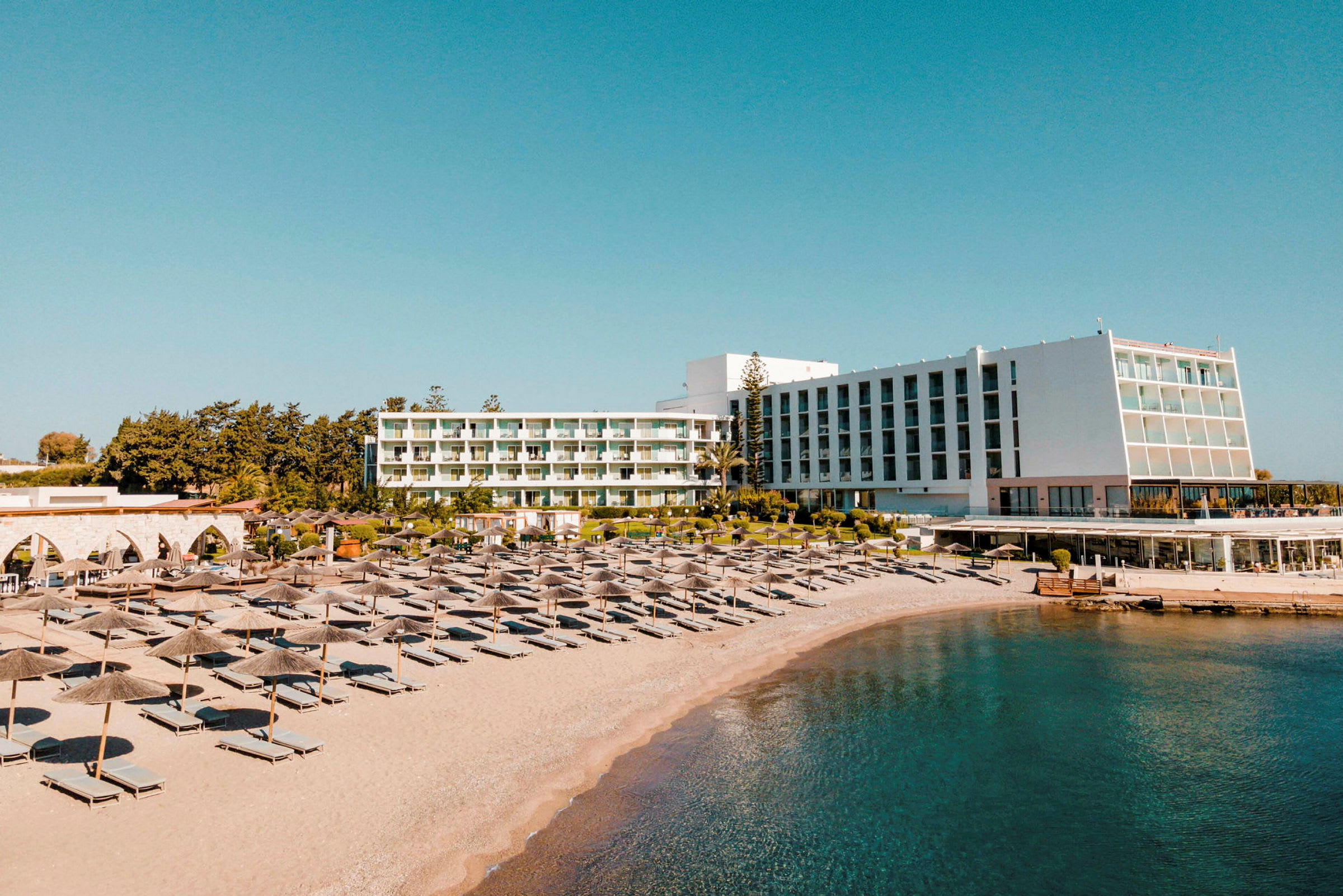Udsigt over hotellet og stranden med liggestole og parasoller. (AI-genereret tekst)