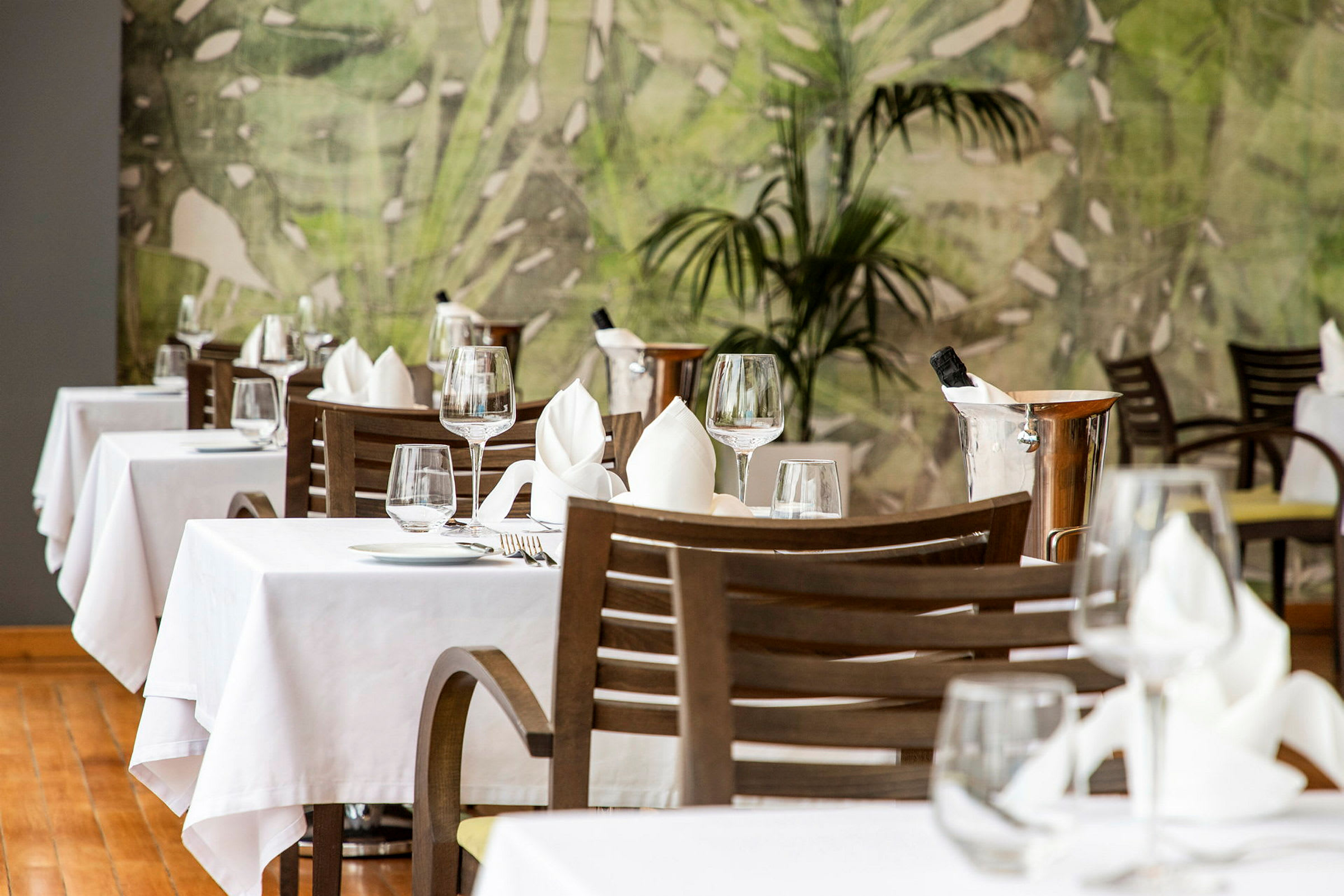 Restaurant med bord dækket med hvid dug, glas og bestik. Grøn baggrund. (AI-genereret tekst)