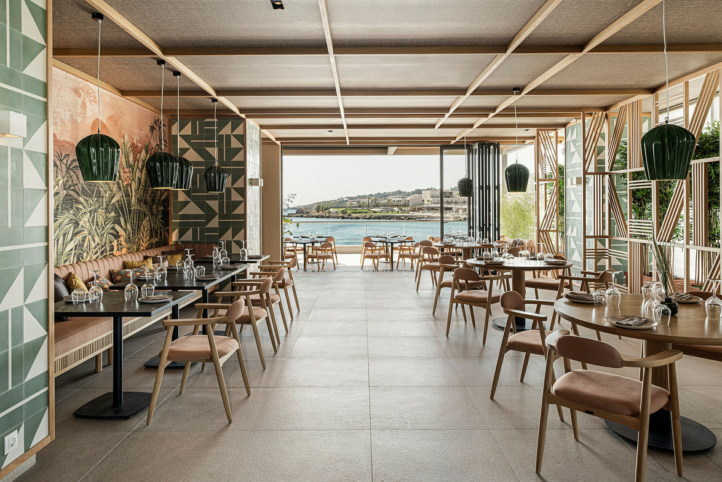 Interiør af en restaurant med borde og stole, stor glasåbning og udsigt over vandet. (AI-genereret tekst)