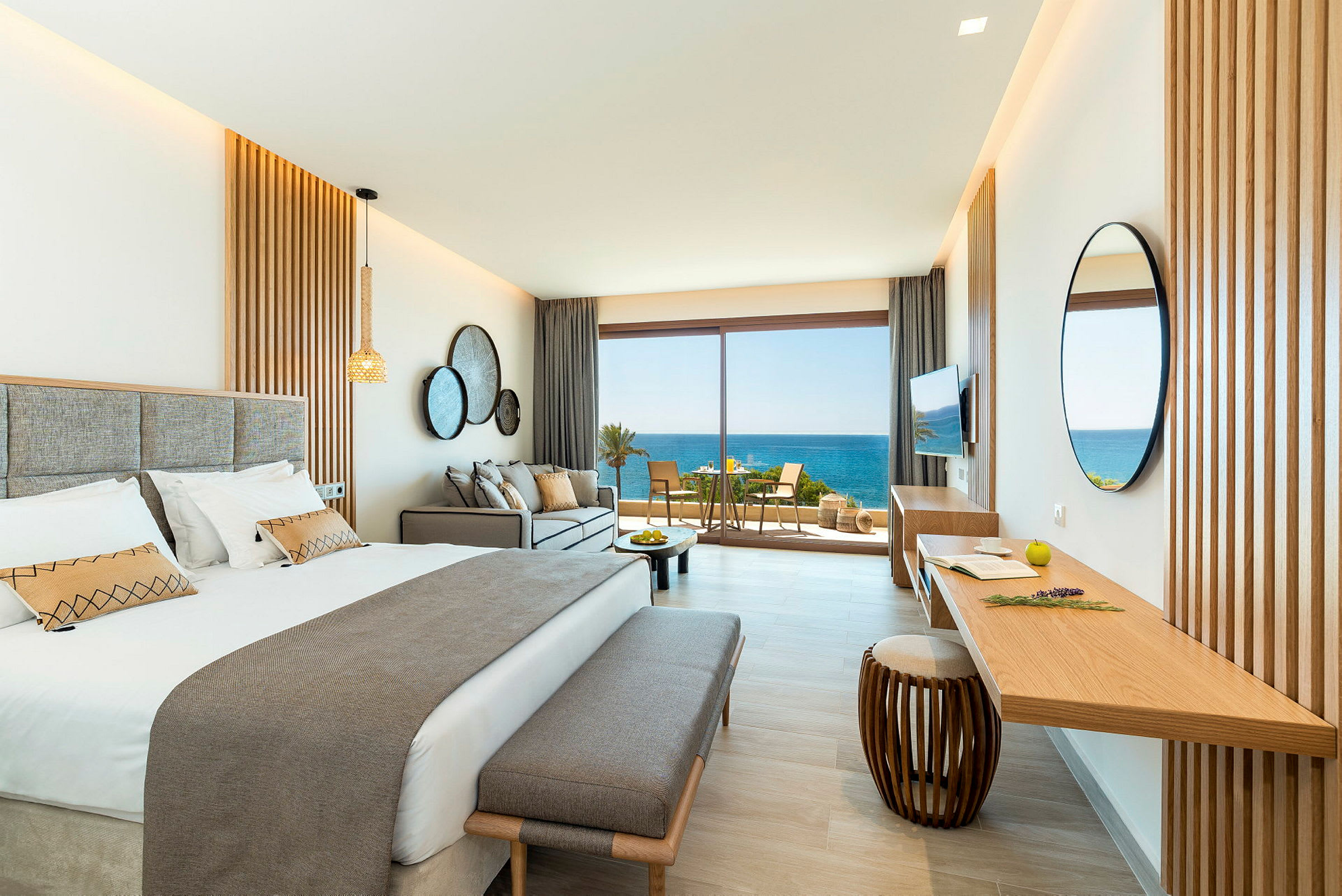 Et stilfuldt hotelværelse med en dobbeltseng, sofa og et skrivebord. Store glasdøre åbner ud til en altan med udsigt over havet. (AI-genereret tekst)