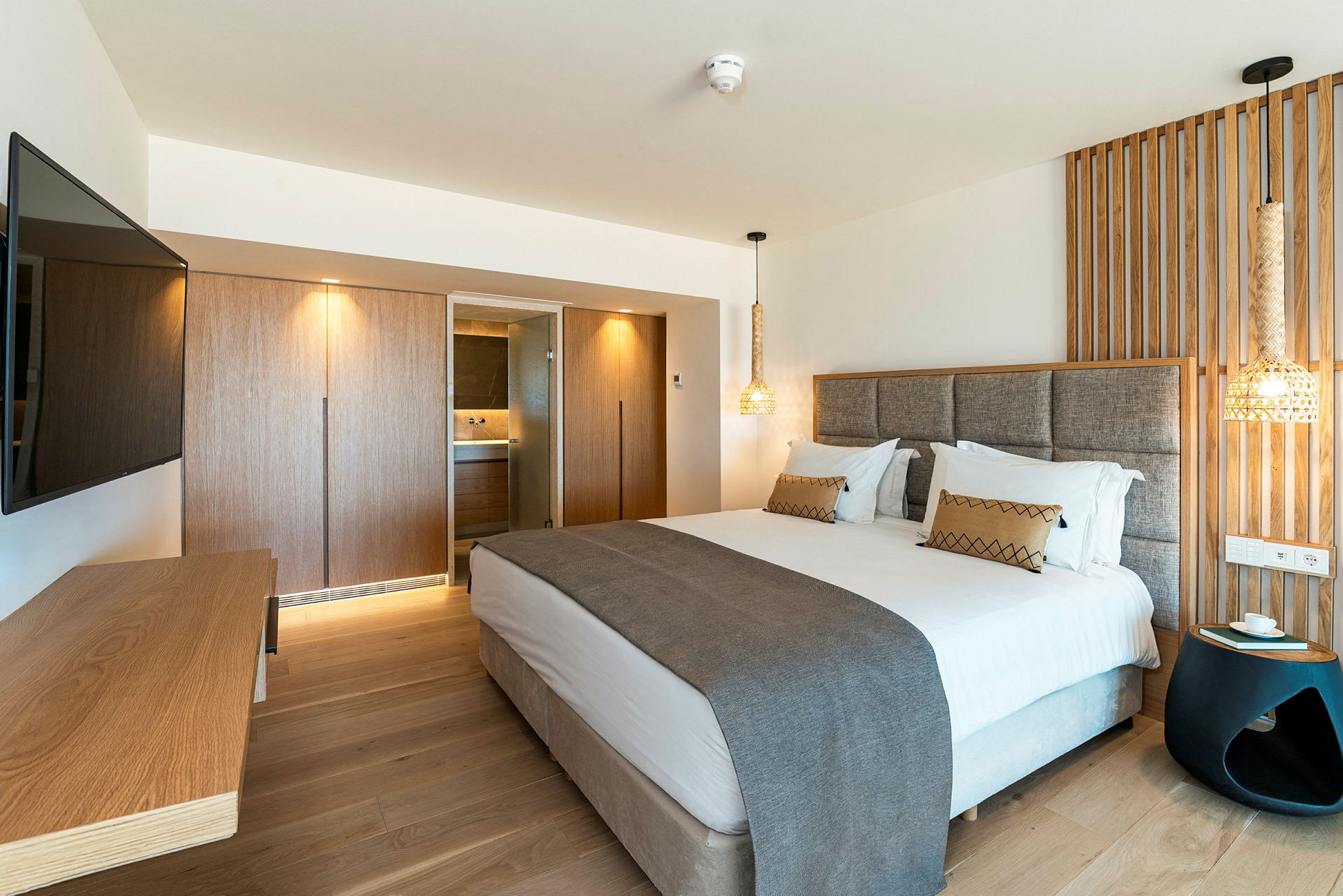 Et moderne hotelværelse med en dobbeltseng, et vægmonteret TV, en træpanel bag sengen og et skrivebord. (AI-genereret tekst)