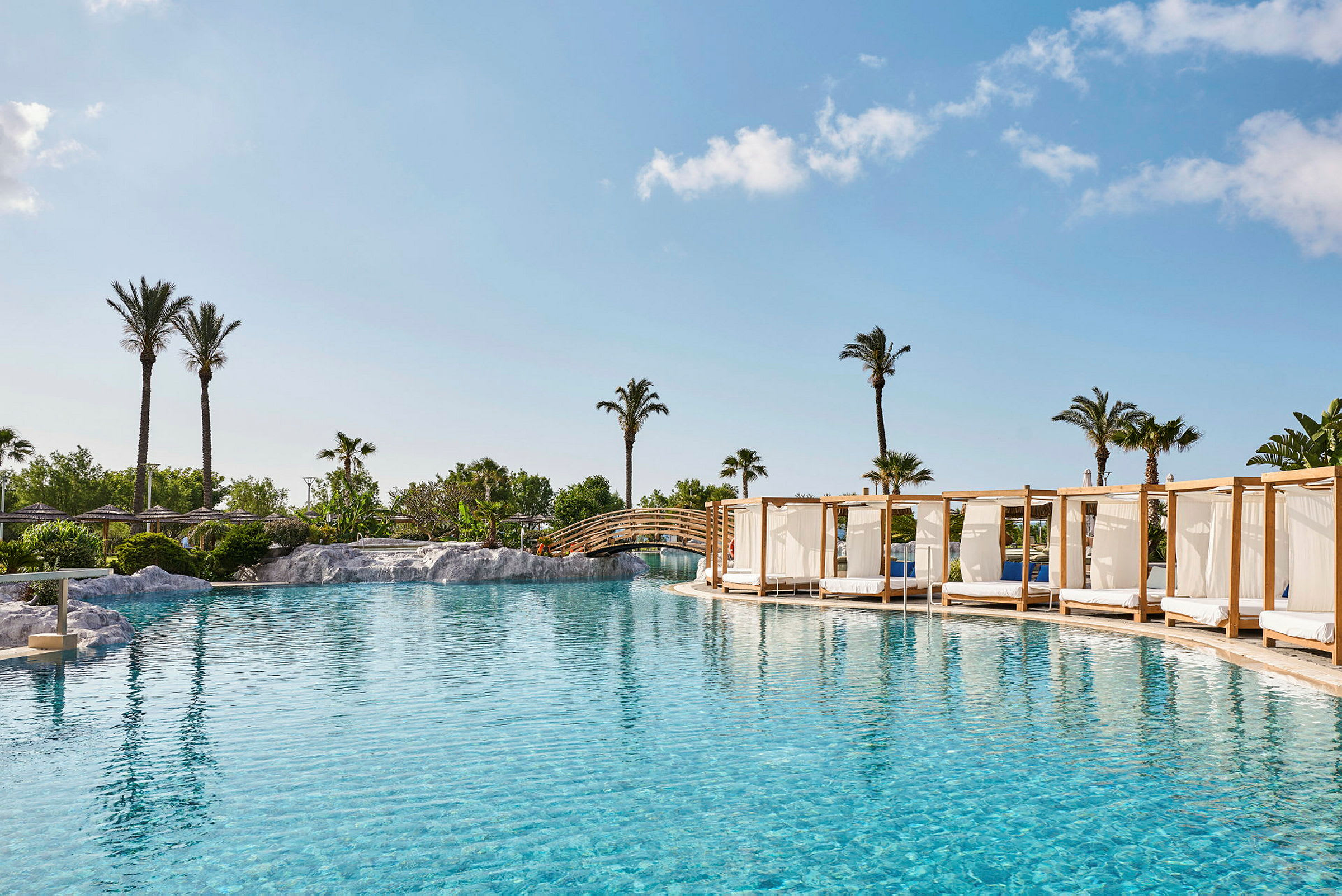 En udsigt over en solrig udendørs swimmingpool omgivet af palmer og cabanas. (AI-genereret tekst)