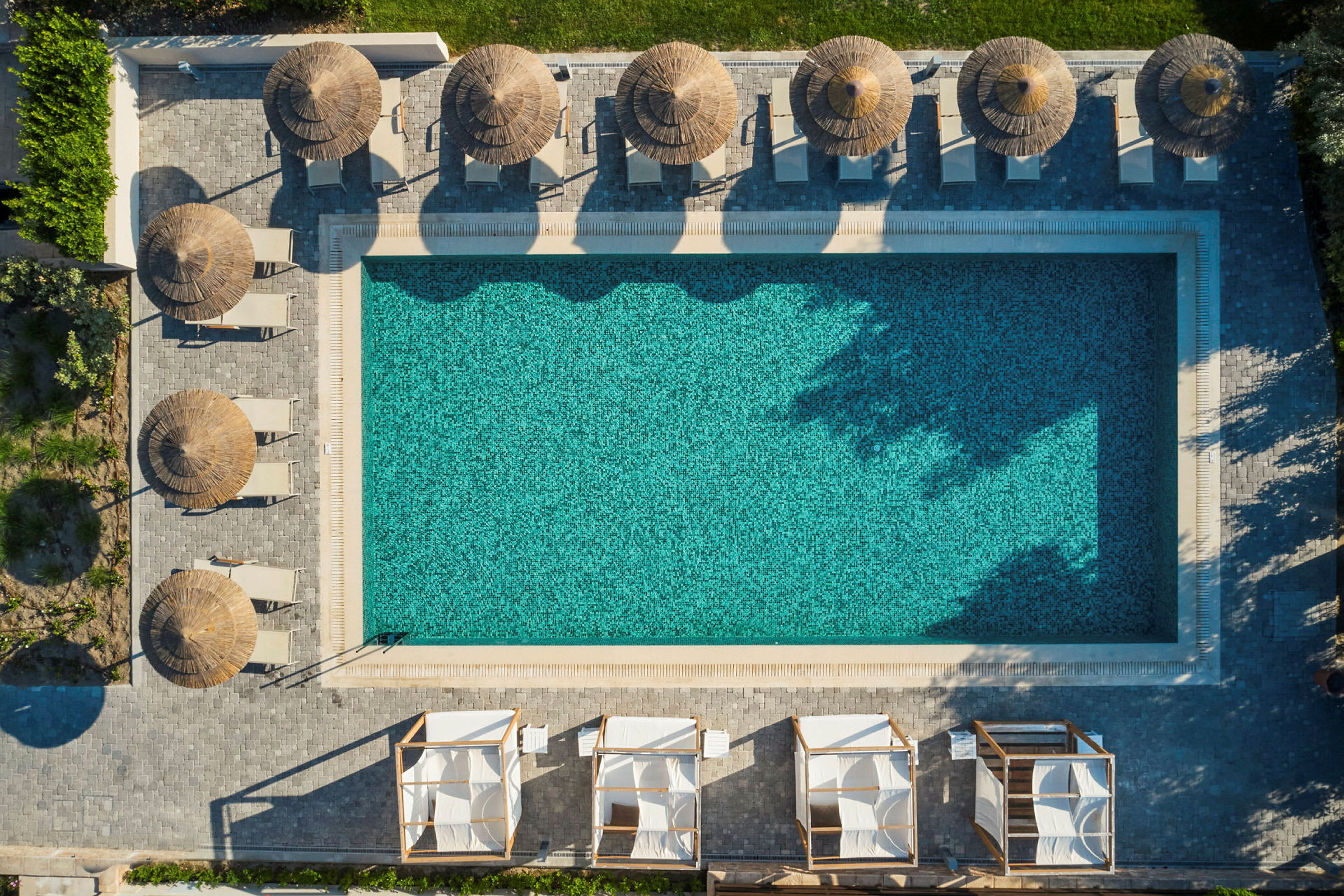 Luftfoto af en rektangulær pool omgivet af parasoller og liggestole. (AI-genereret tekst)