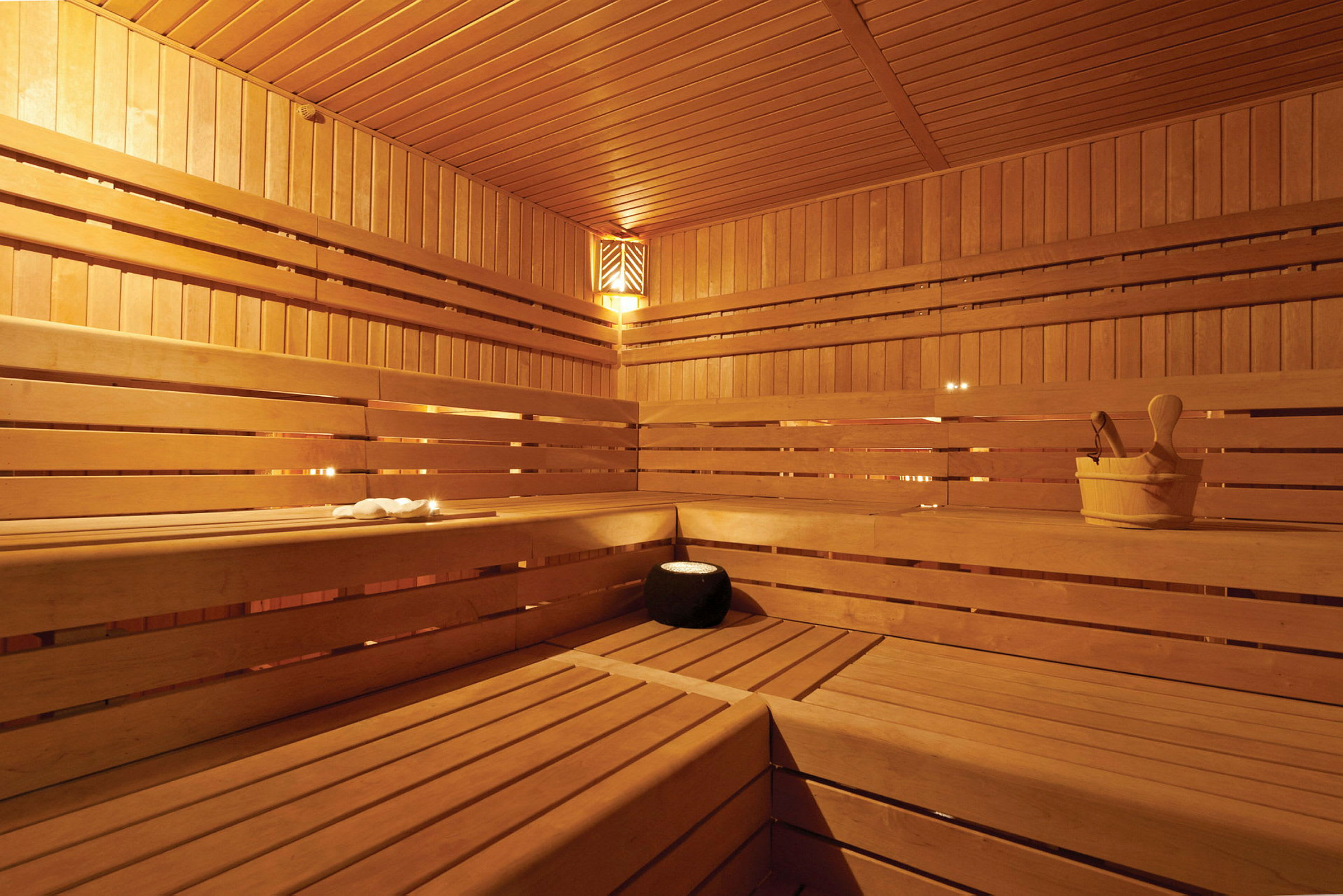 En sauna med træbænke og træpaneler samt en spand og en skovl. (AI-genereret tekst)