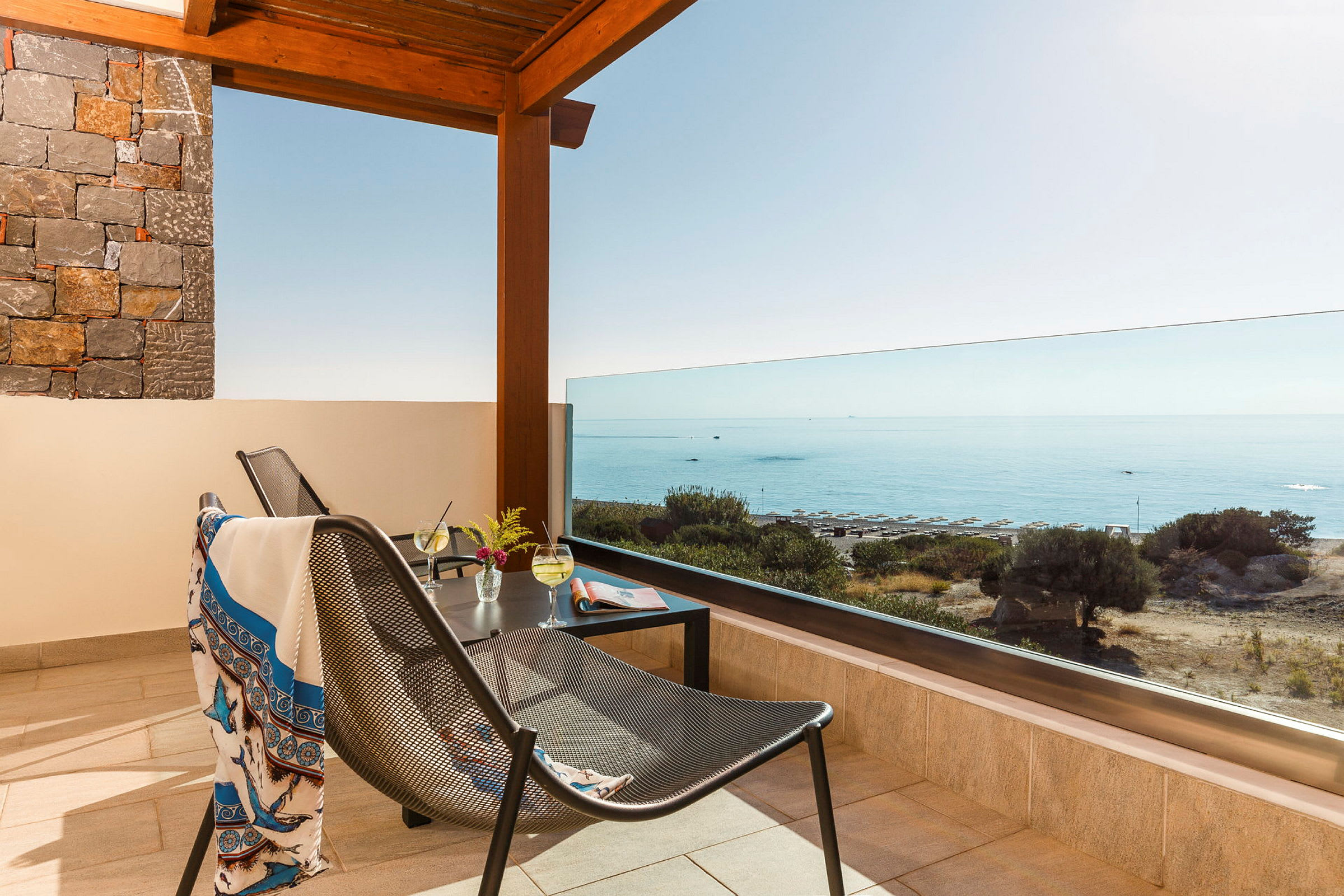 Terrasse med udsigt over havet, møbler og drikke på bordet. (AI-genereret tekst)