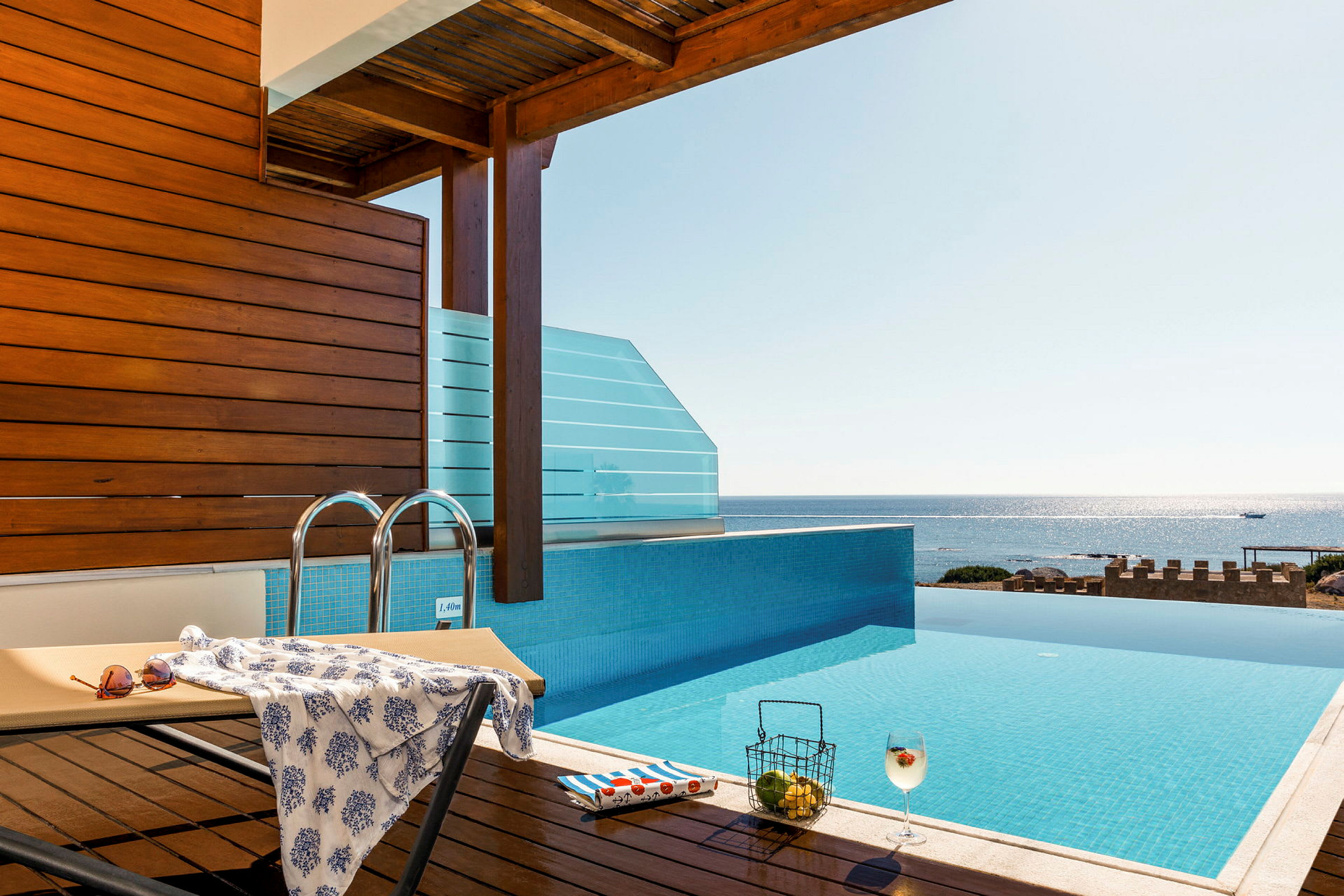 En infinity-pool med udsigt over havet, en liggestol og en drink. (AI-genereret tekst)