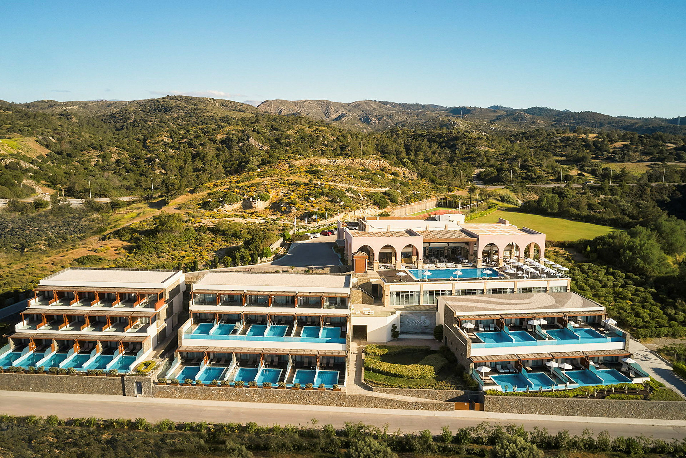 Hotelkompleks med flere bygninger og private pools, beliggende i naturligt landskab med bjerge og vegetation. (AI-genereret tekst)