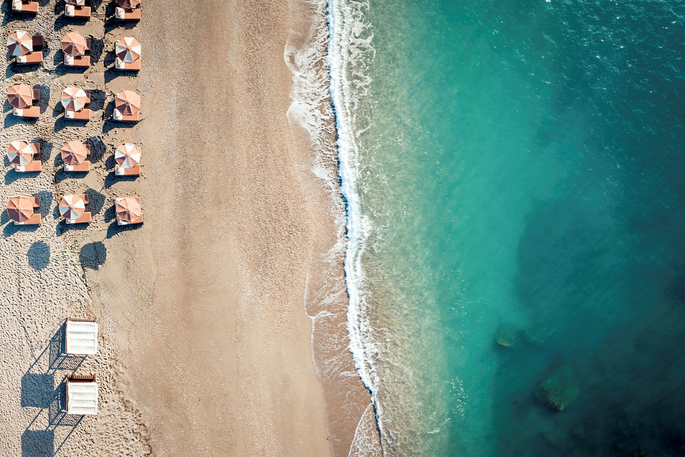 Luftfoto af en strand med parasoller og turkisblåt vand. (AI-genereret tekst)