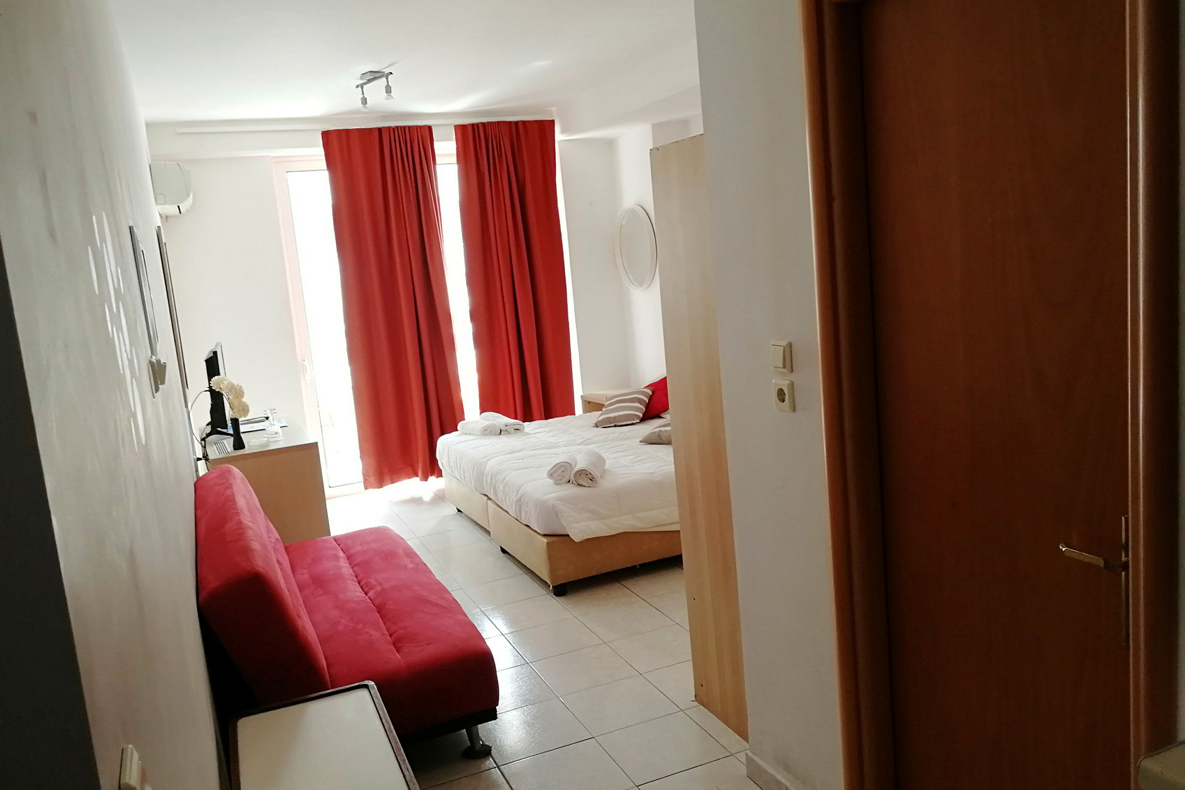 Et hotelværelse med en opredt seng, røde gardiner og en rød sofa. (AI-genereret tekst)