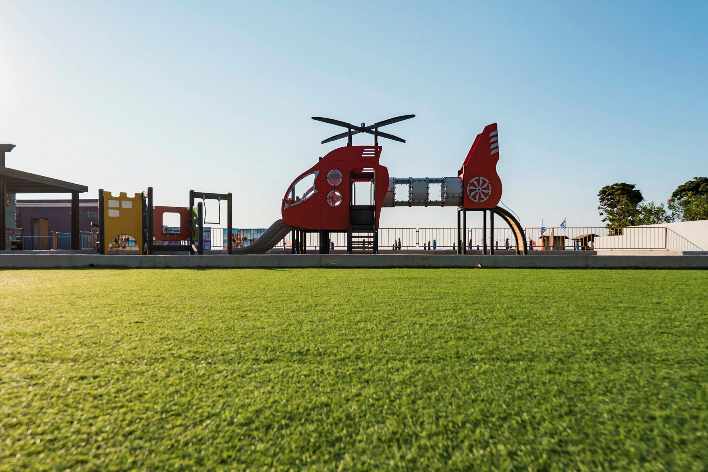 Legeplads med helikopterformede legestrukturer og frodig græsplæne. (AI-genereret tekst)