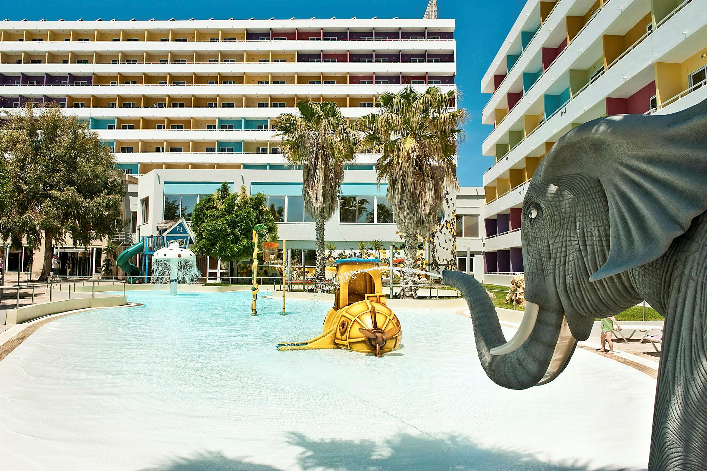 Børnepool med elefantfigur og legeskulpturer ved hotelkompleks. (AI-genereret tekst)